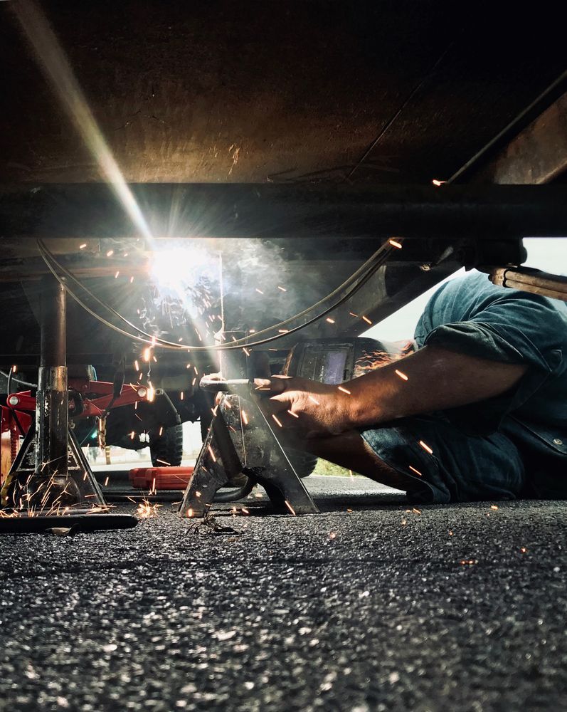 A Man is Welding Under a Car on the Ground — Ace Exhaust Centre in Berserker, QLD