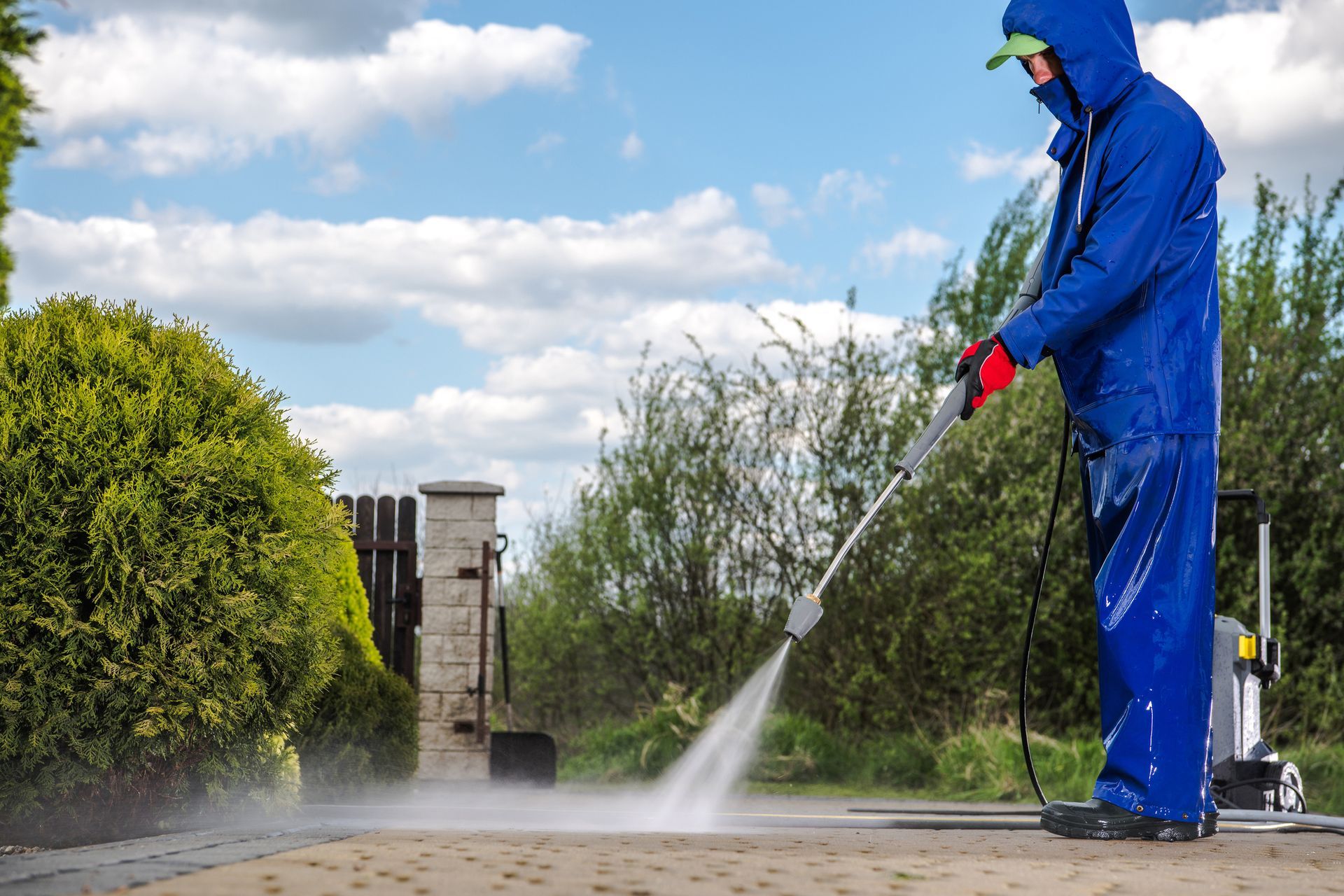 Man in a blue raincoat using a pressure washer to clean an outdoor surface.