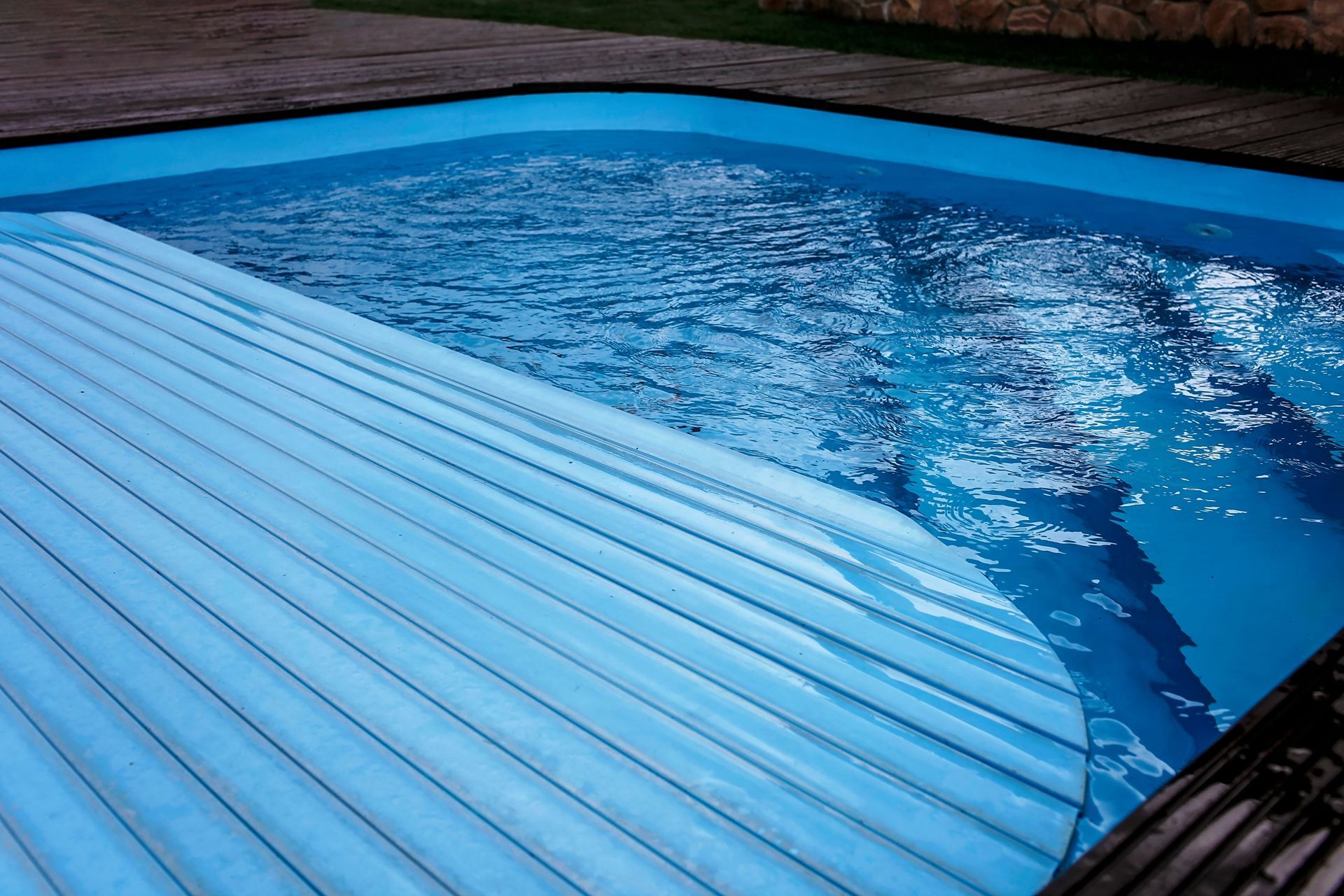 Pool with partially open blue cover, water reflecting ambient light.