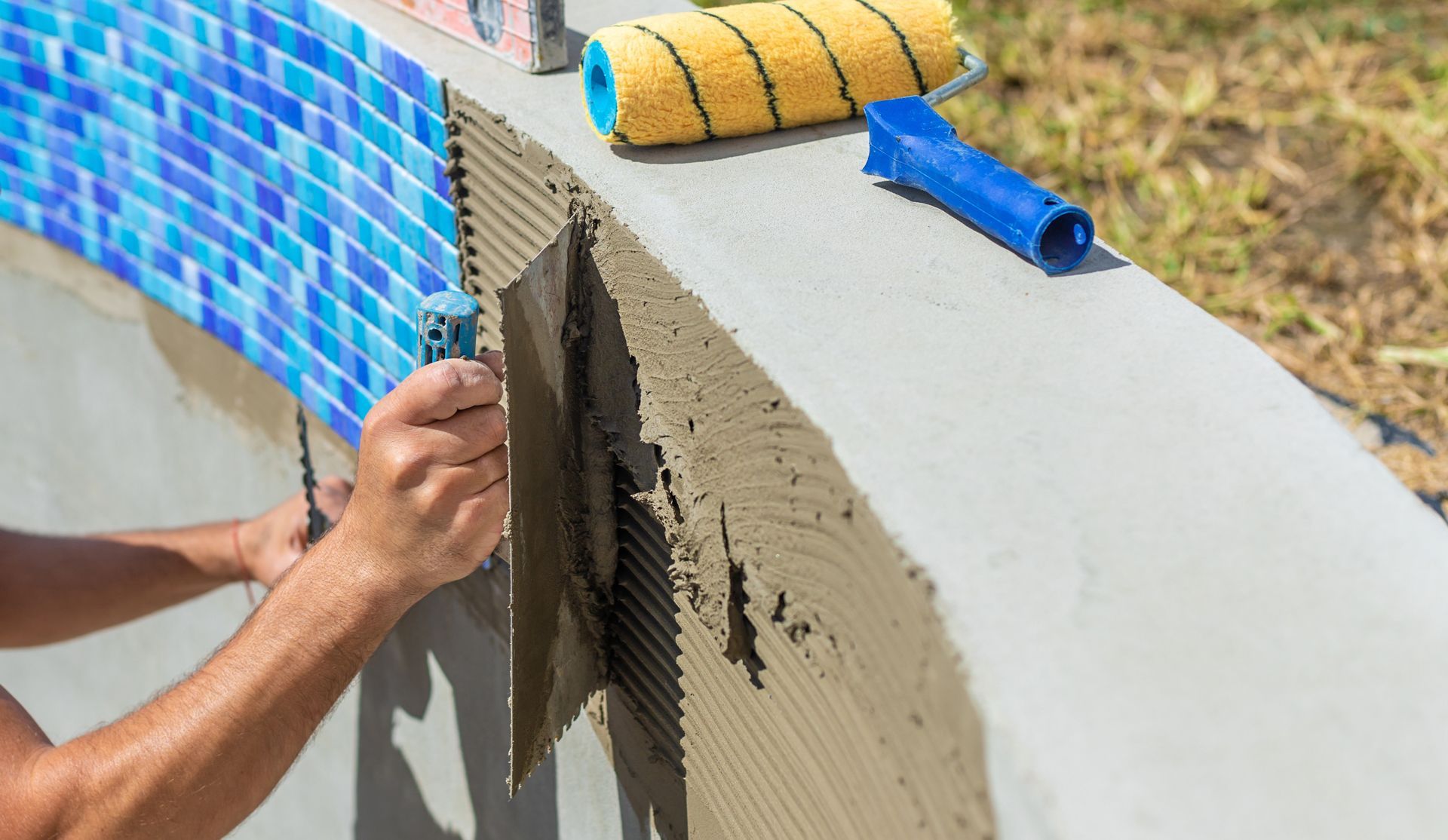 Person tiling a curved pool edge with blue mosaic tiles. 