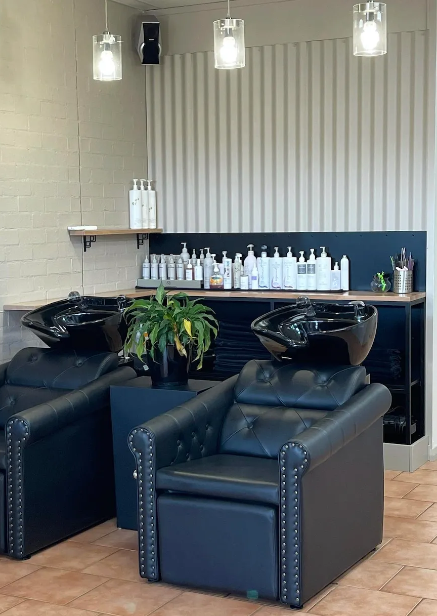 Two black shampoo chairs with integrated bowls in a modern salon with neutral walls and soft pendant lighting. — Devyani Hair & Beauty in Unanderra, NSW