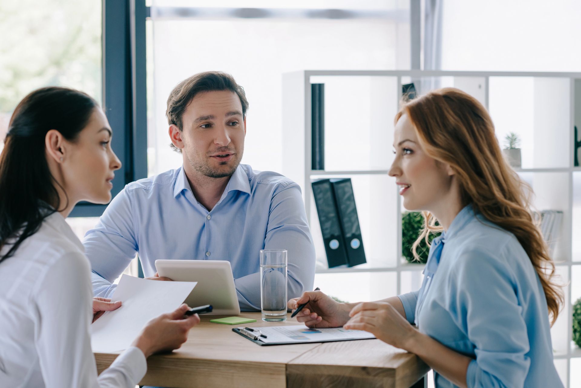 Three coworkers in a bright office discussing a tablet and papers around a round table