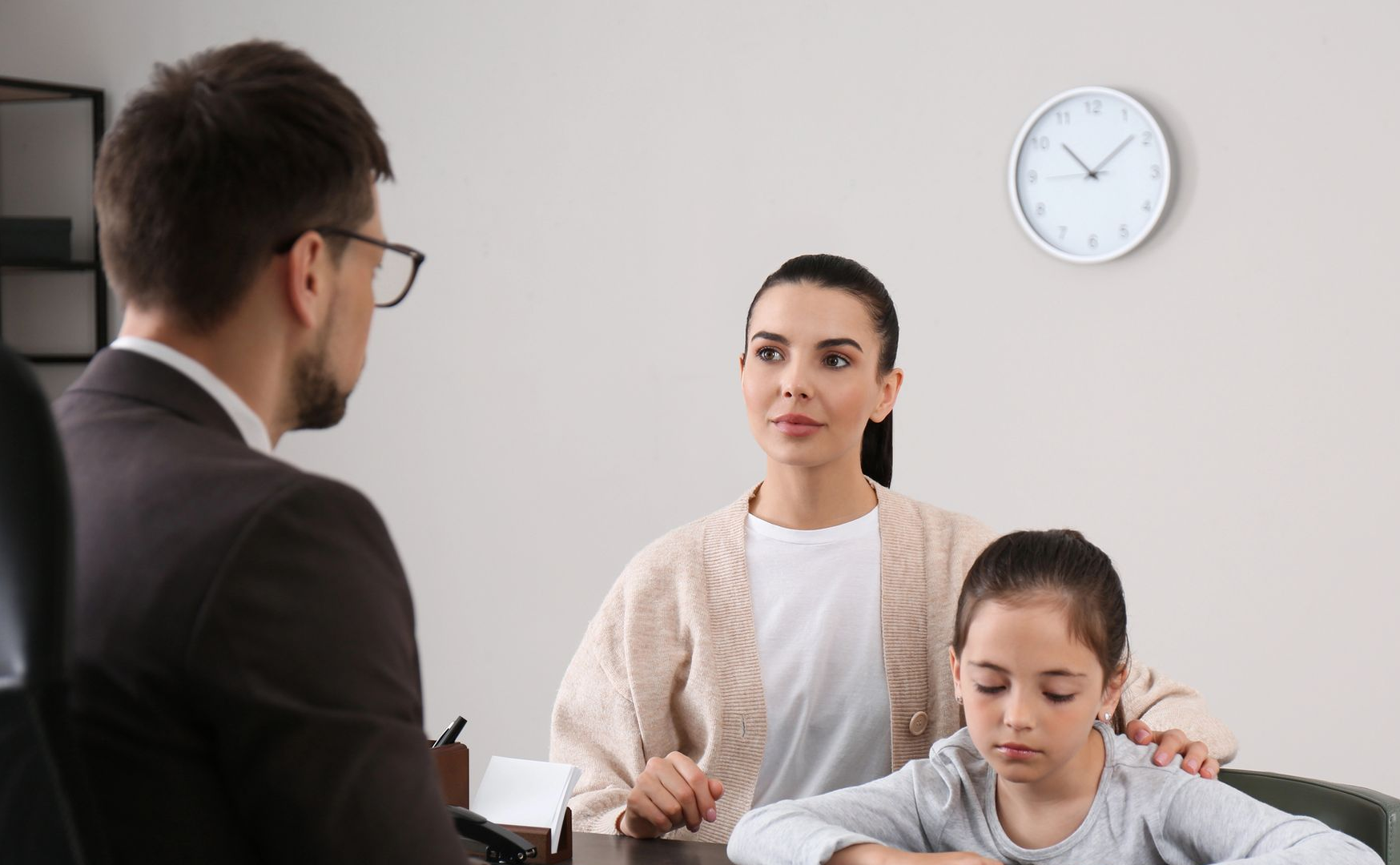 Three people at a desk in a meeting room, with a clock on the wall.