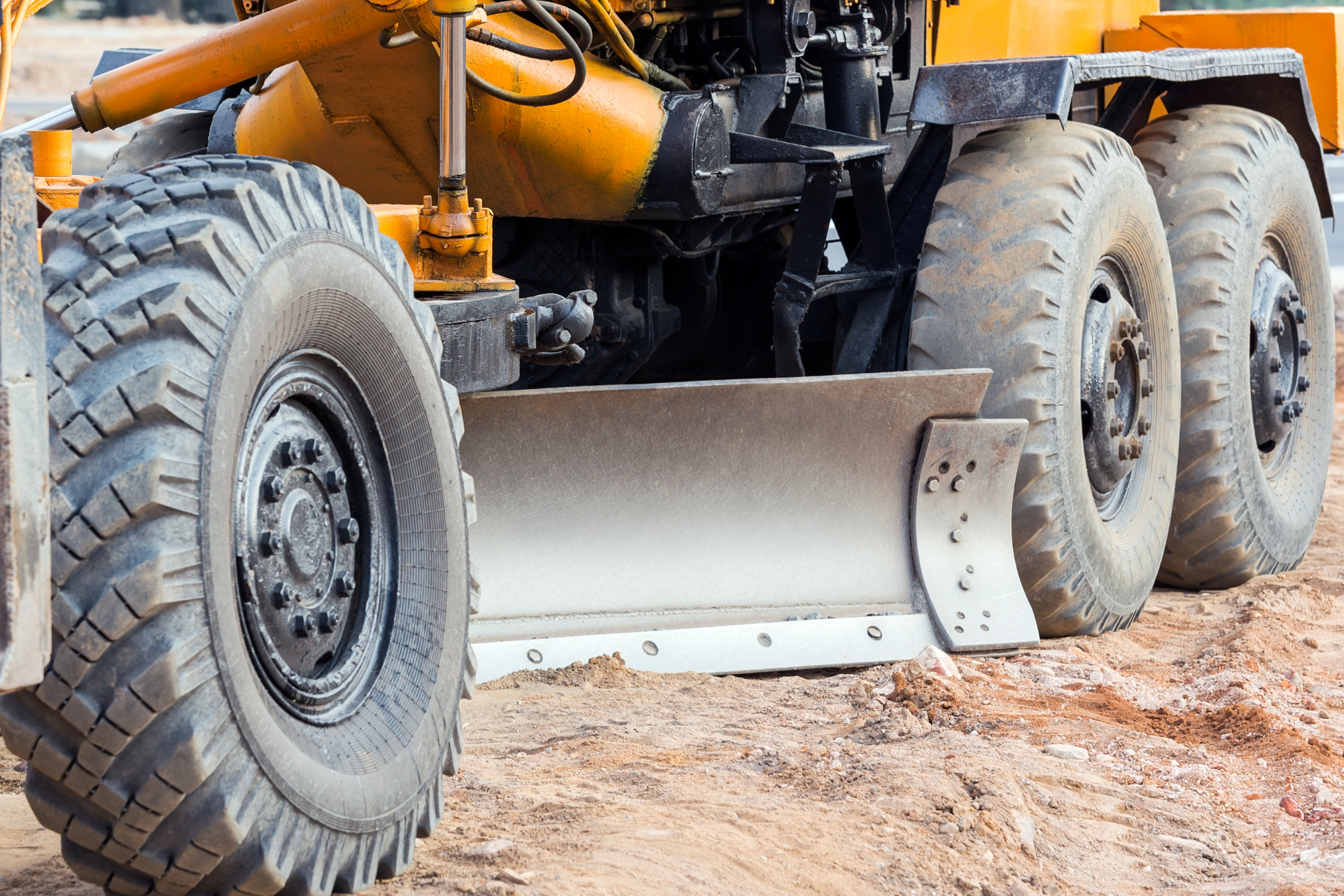 Yellow road grader with large tires leveling dirt on a construction site