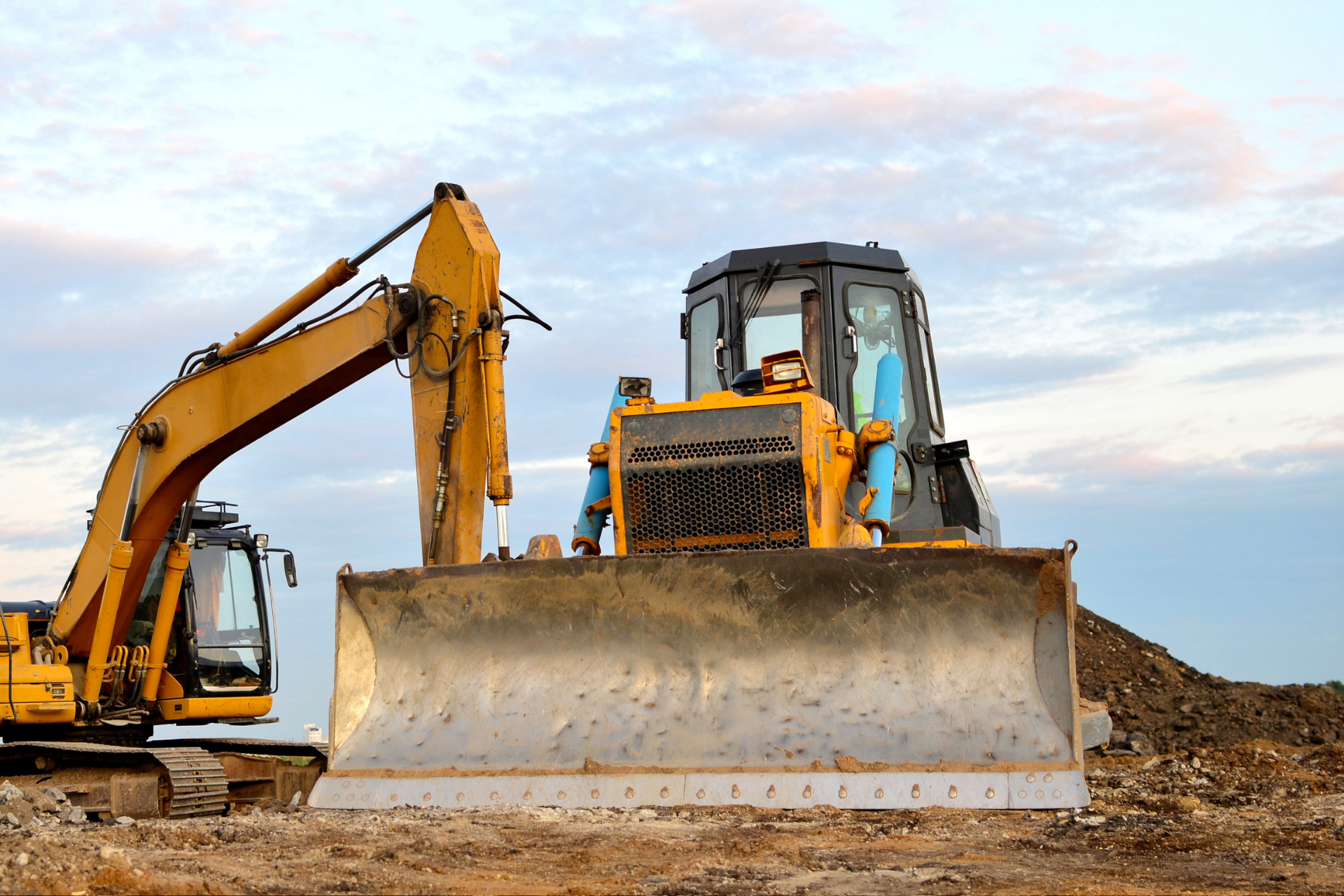 Yellow bulldozer and excavator at a construction site under a cloudy sky