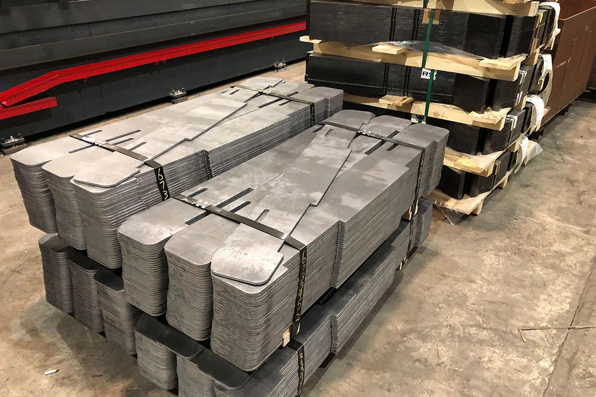 Stacked metal bars bound with straps on pallets in a warehouse aisle.