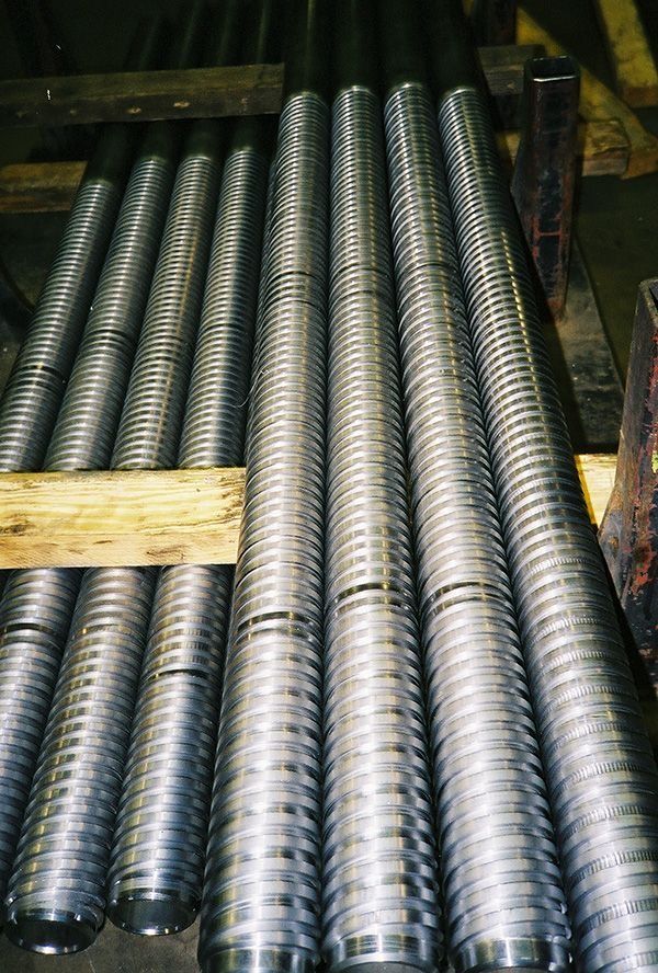 Rows of shiny silver corrugated metal pipes stacked together in a warehouse-like setting