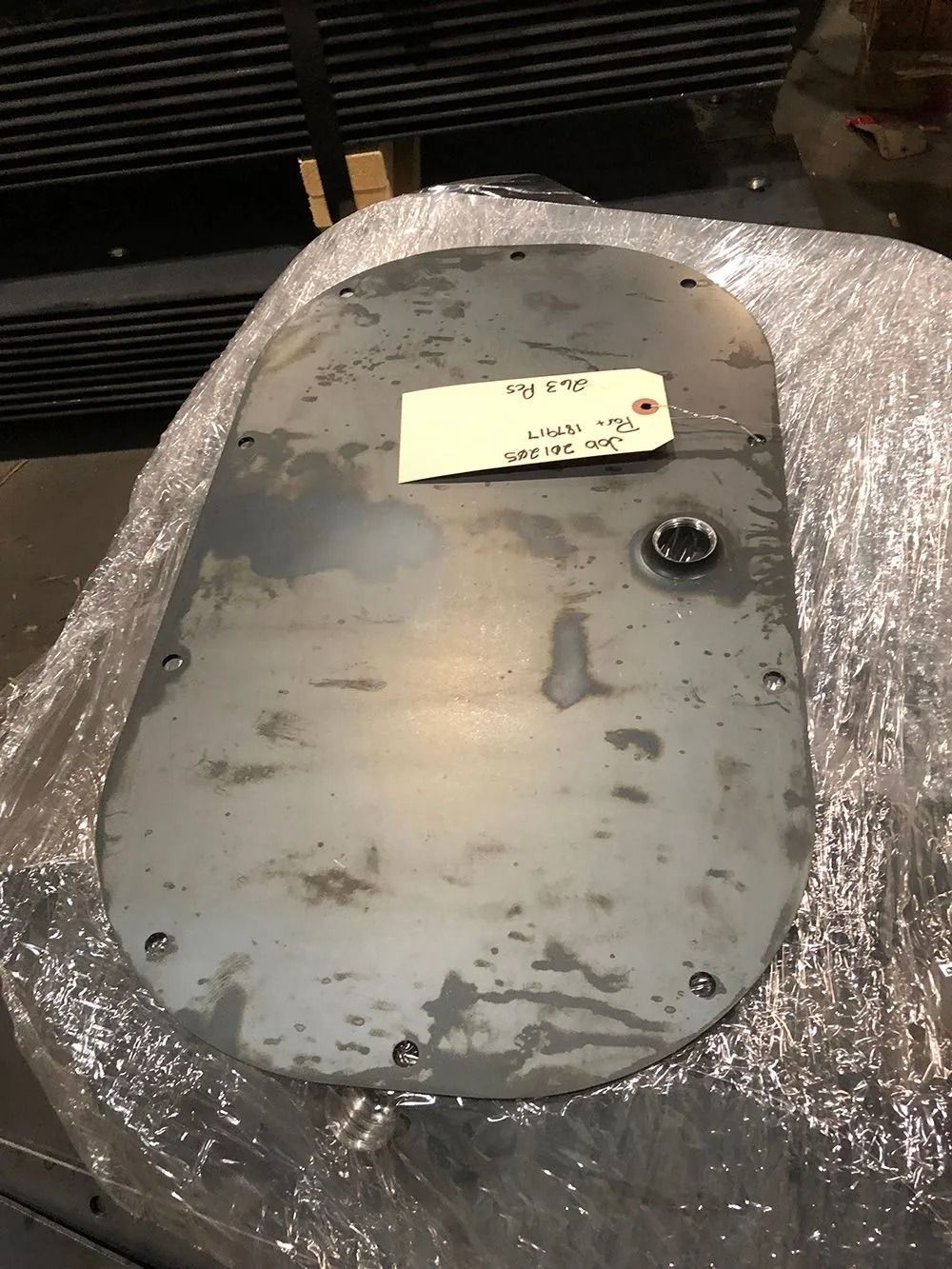 Gray metal panel wrapped in bubble wrap, with a small note and a circular fitting on top.