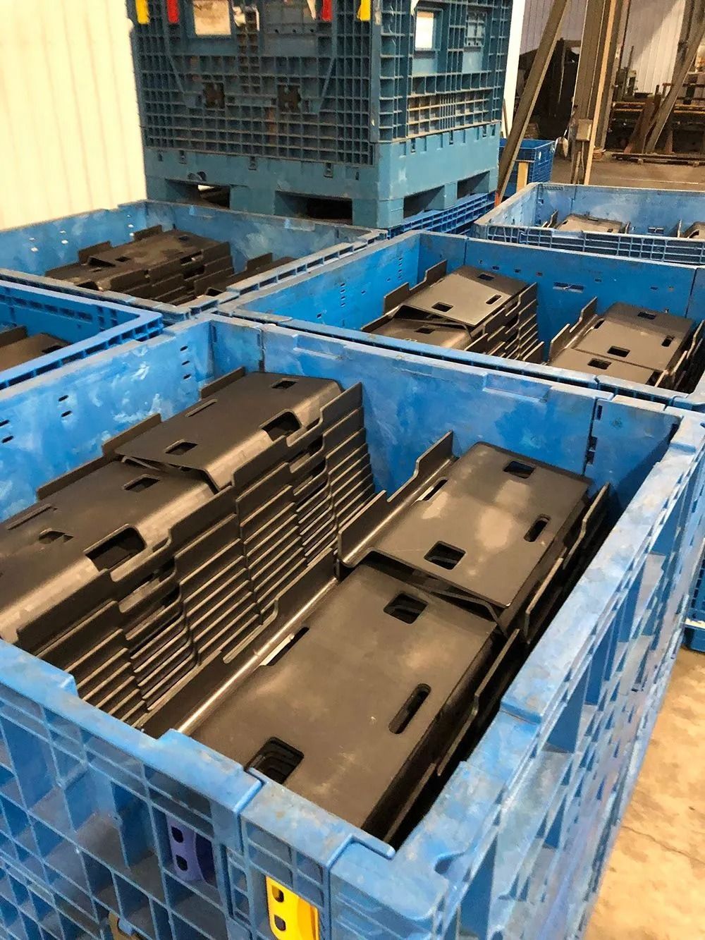 Stacked black plastic parts in blue industrial bins on a factory floor
