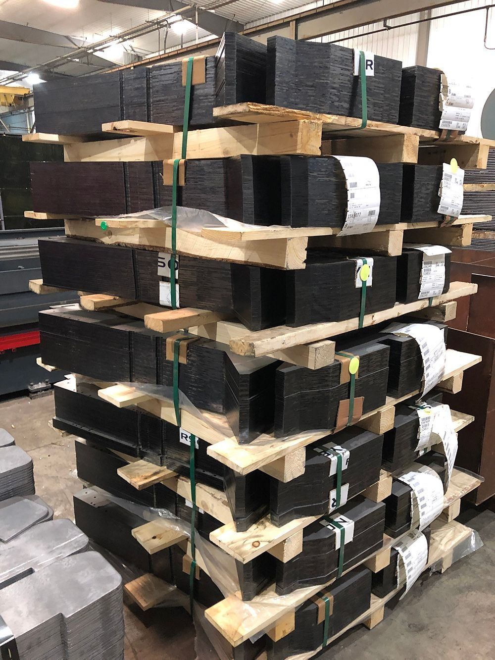 Stacked pallets of black rectangular items strapped with white bands in a warehouse aisle.