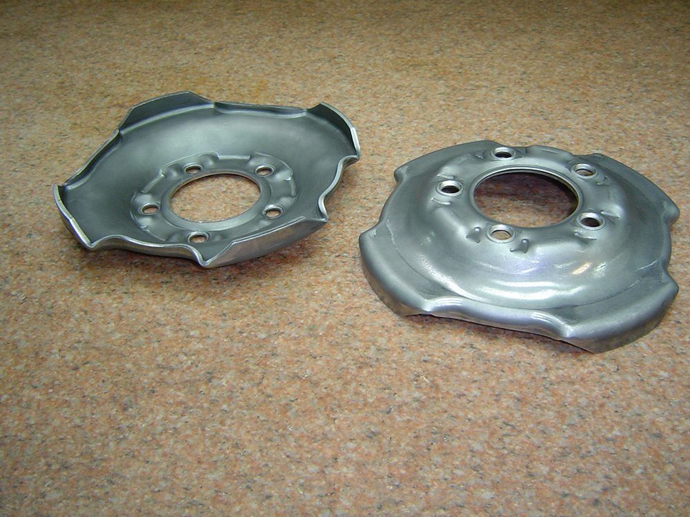 Two metal wheel hubcaps on a tan carpet, one darker and one shiny silver.