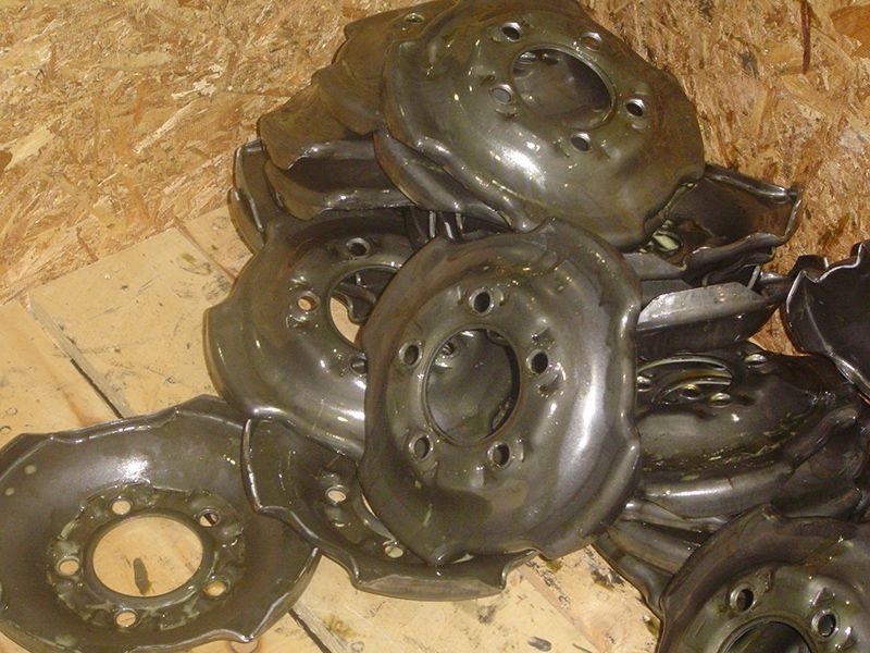 Pile of black metal circular parts on a wooden surface, with bolts and central openings.