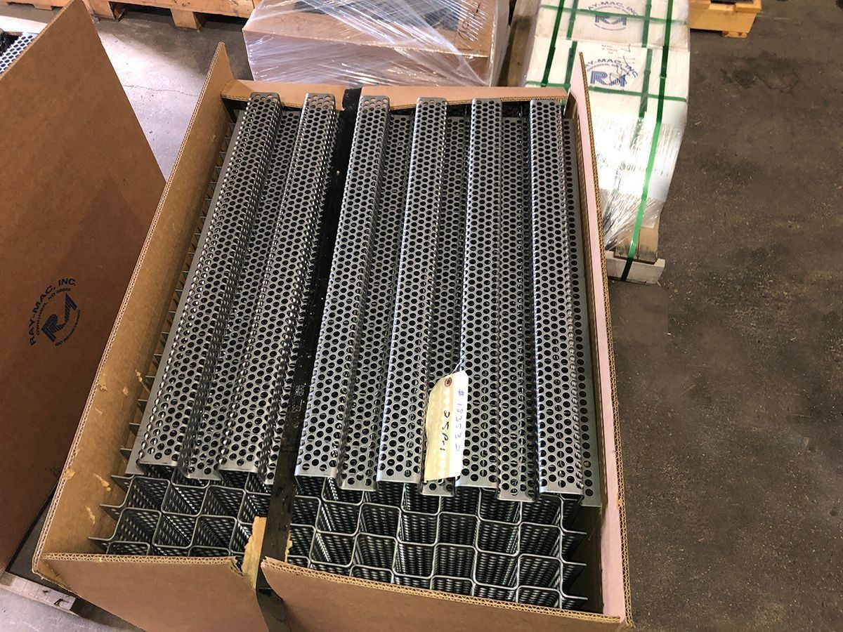 Cardboard box filled with stacked black metal mesh trays in a warehouse setting