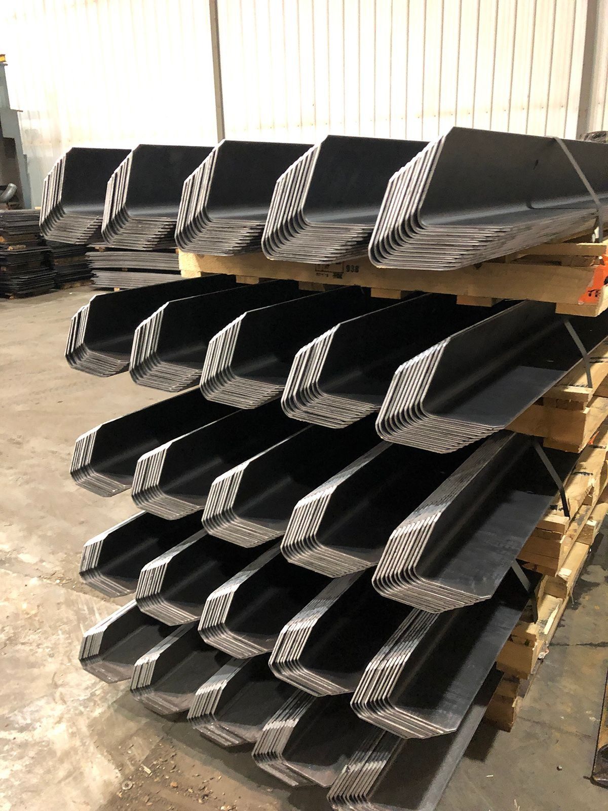Stacks of black corrugated plastic or metal parts on wooden pallets in a warehouse.