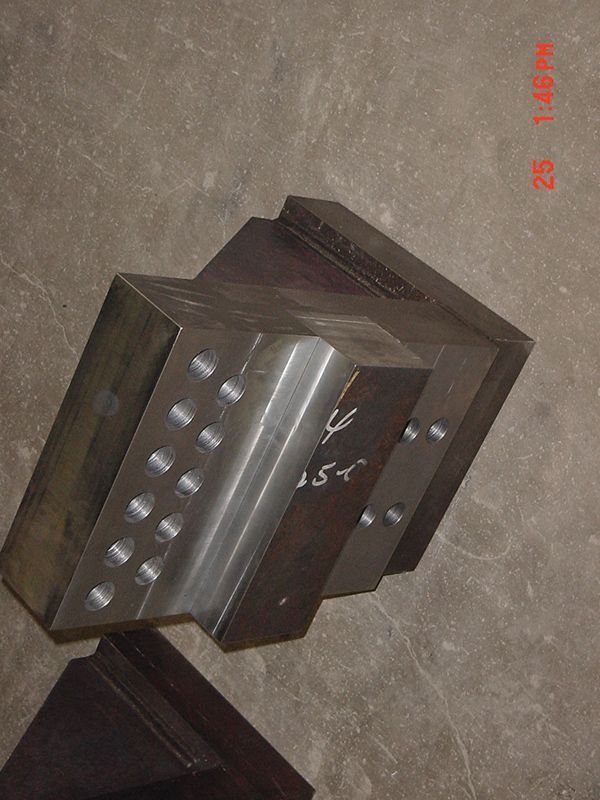 Dark metal industrial part with bolts on a concrete floor, viewed at an angle