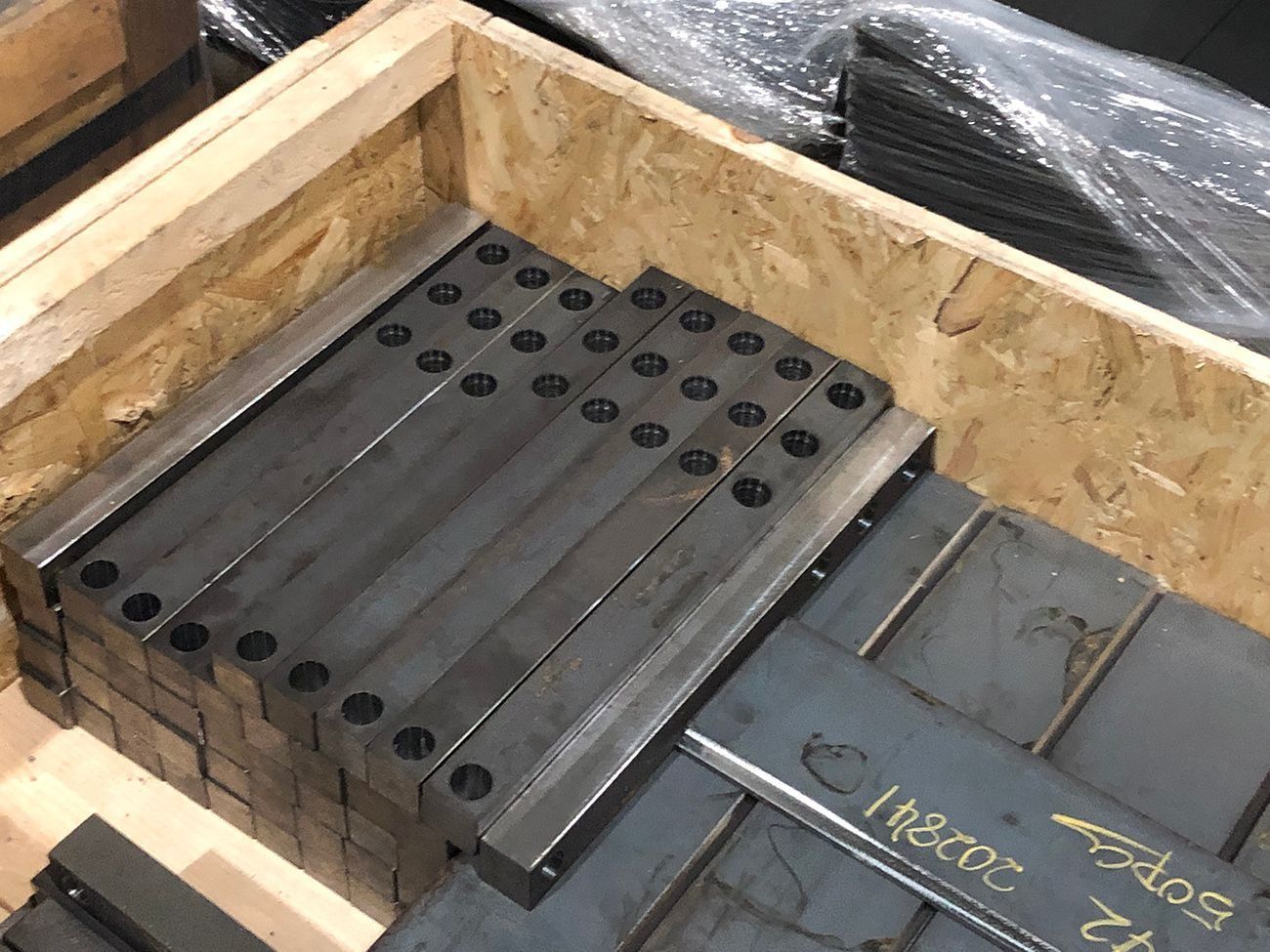 Stacked metal machine parts in a wooden crate, with a dark gray plate on top.