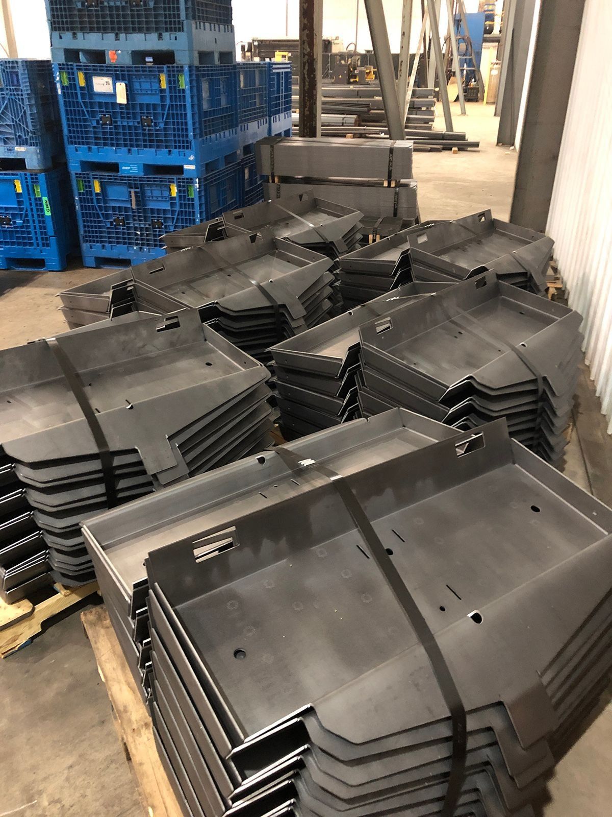 Stacks of black plastic trays in a warehouse beside blue crates and industrial equipment