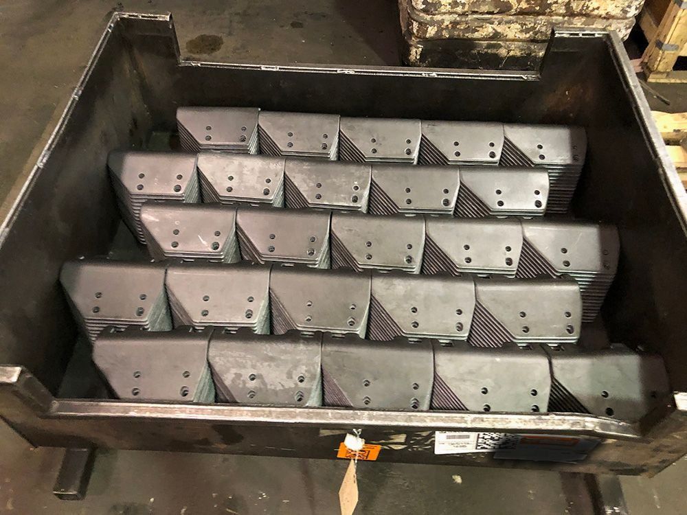 Metal bin filled with rows of gray metal brackets in a workshop container