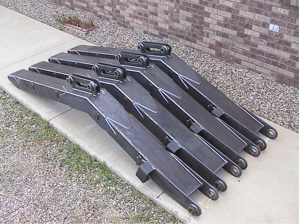 Five black metal lifting forks stacked on a sidewalk beside a brick wall