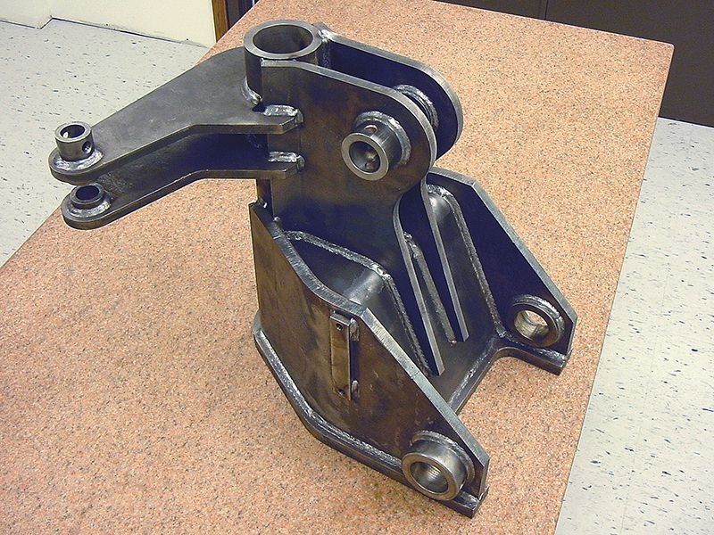 Black metal mechanical bracket or hinge assembly on a tan surface.