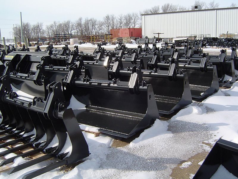 Rows of black excavator buckets lined up outdoors on snowy ground in an equipment yard