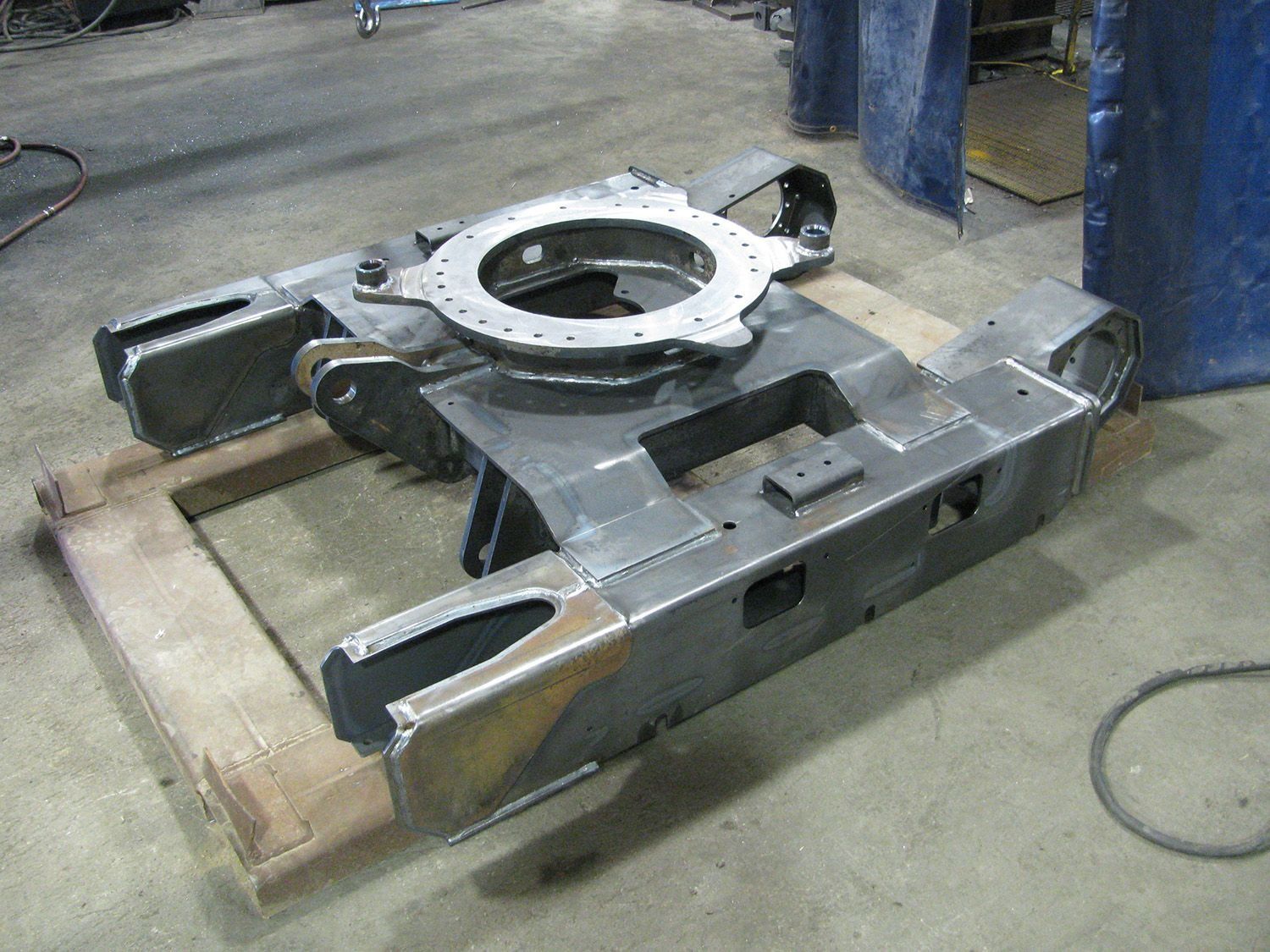 Metal industrial machine part on a pallet in a workshop, with a circular opening and gray-black components.