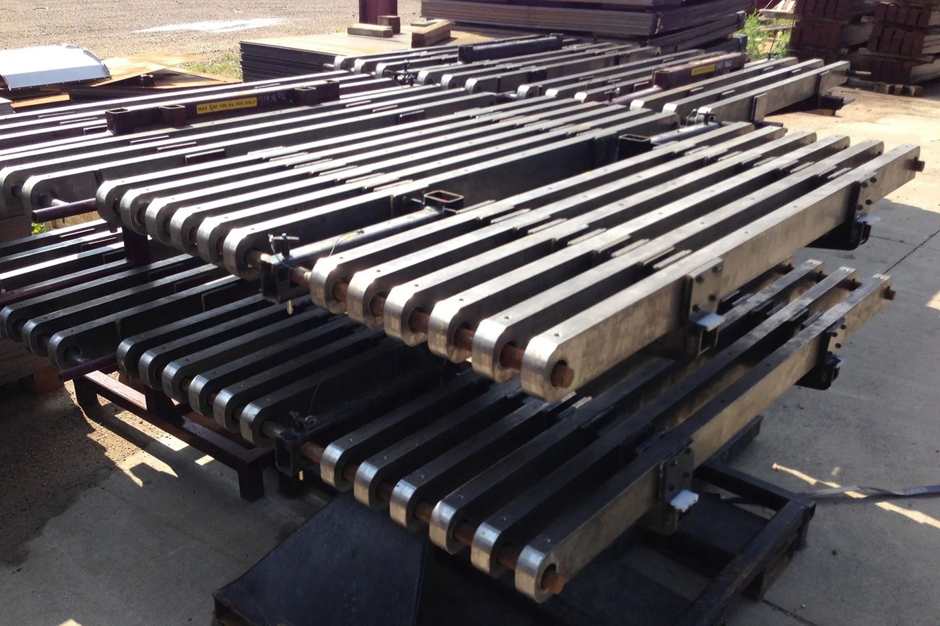 Stacked metal conveyor rollers on pallets in an outdoor industrial yard.