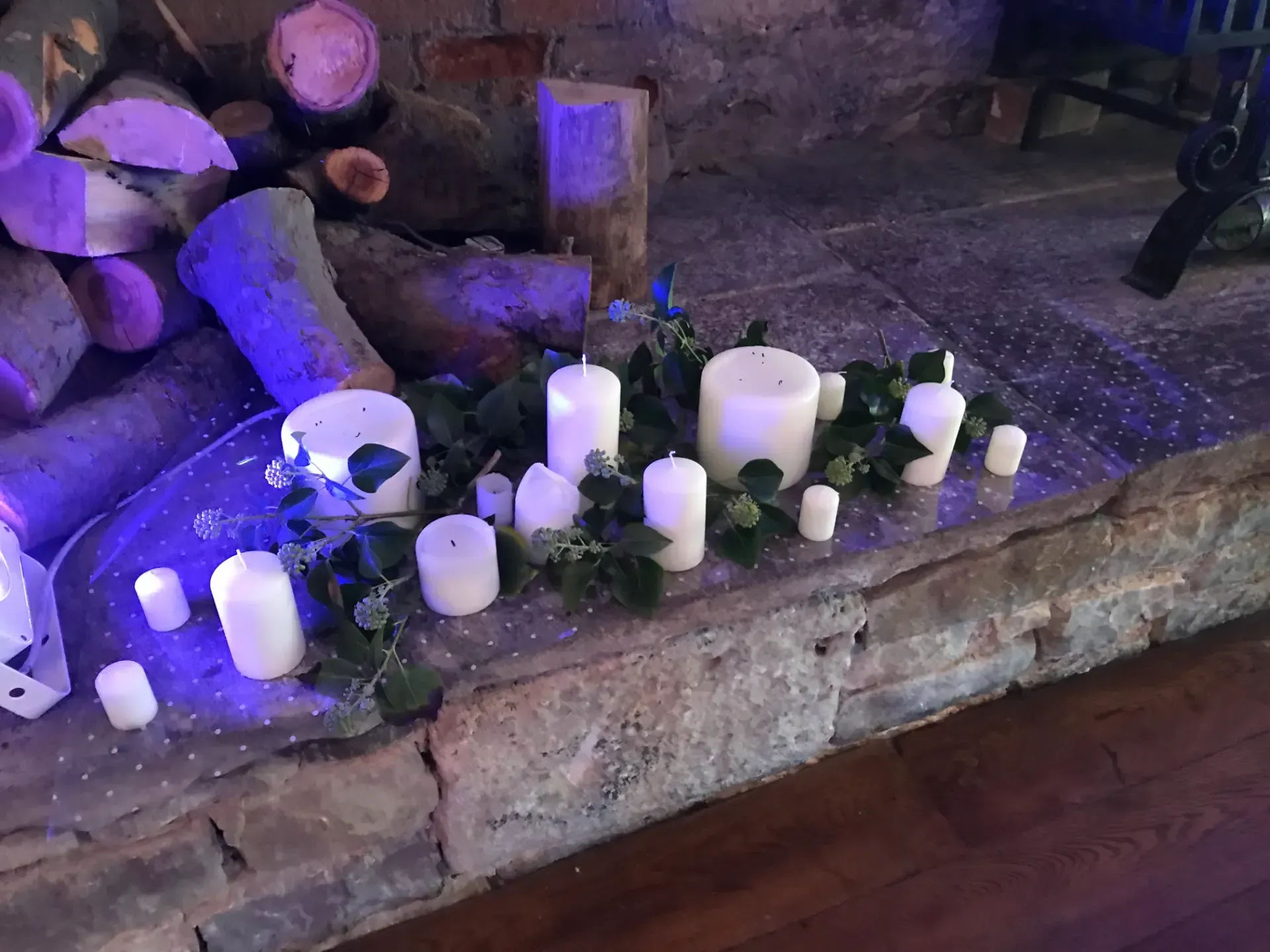 Candles and small flowers arranged on a stone ledge in dim purple light