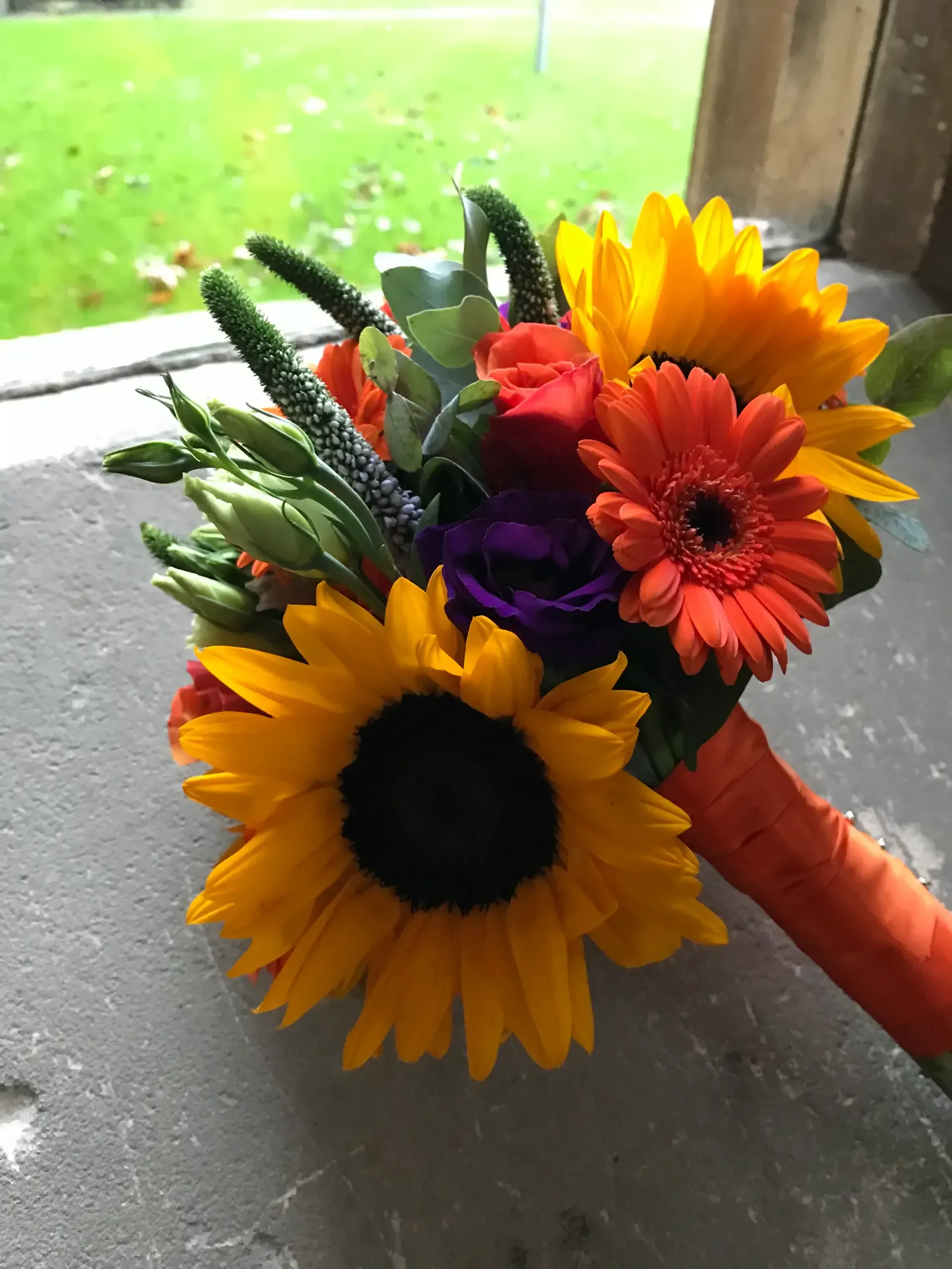 Bright bouquet with sunflowers, orange and red gerbera daisies, and purple flowers on a windowsill