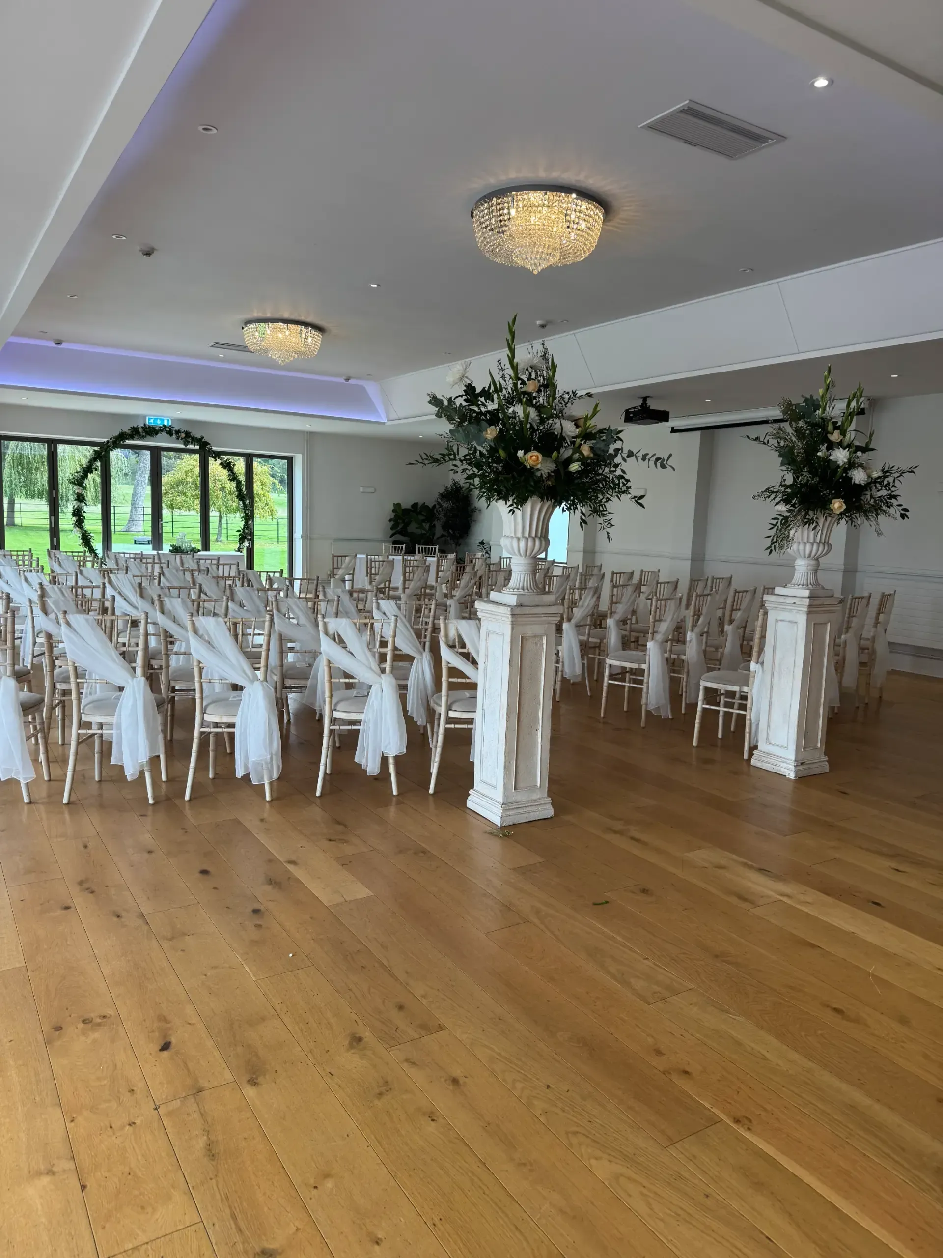 Bright wedding reception hall with white chairs, floral centerpieces, and polished wood floors