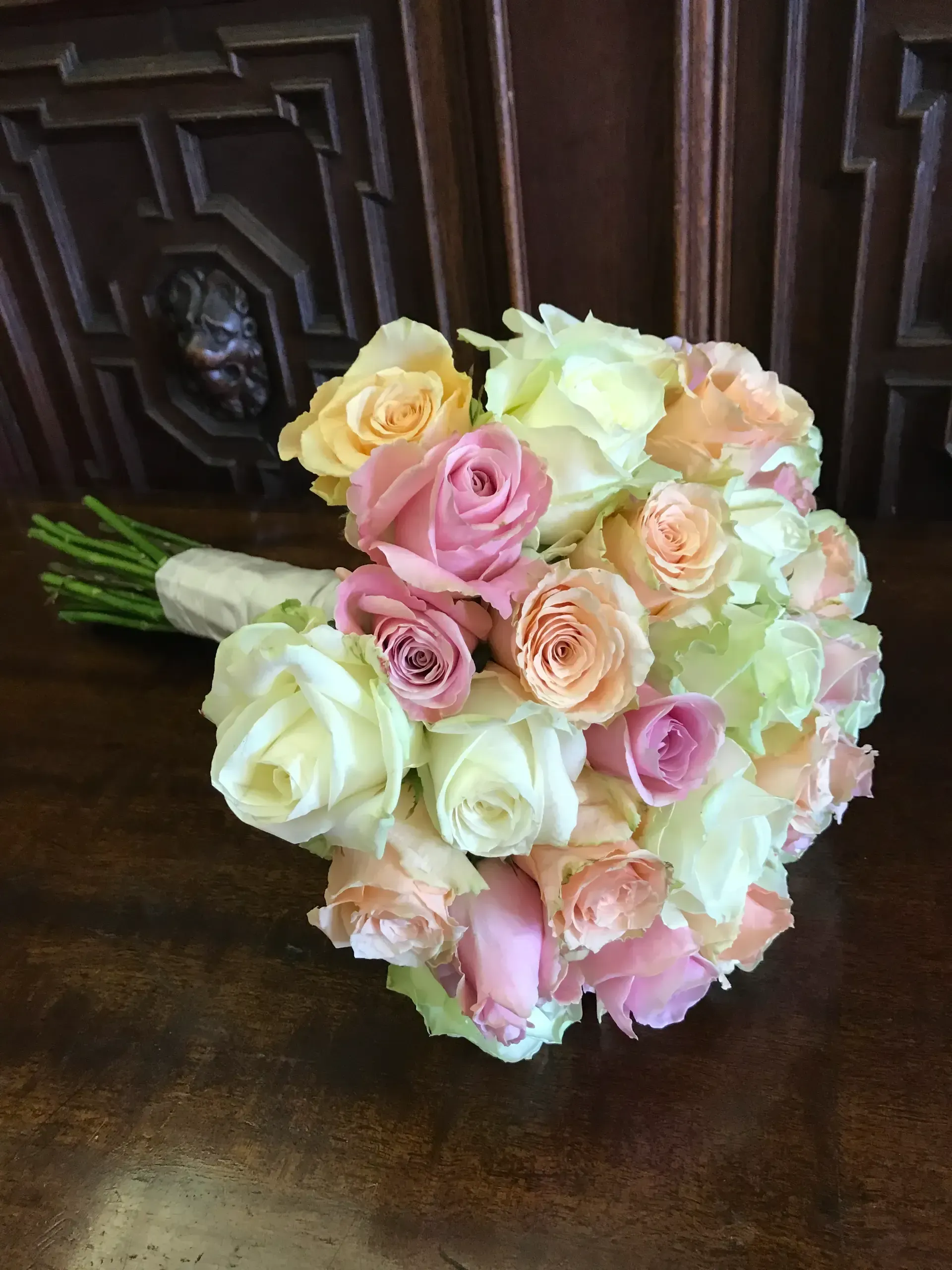 Bouquet of pastel roses in pink, peach, cream, and pale yellow on a dark wooden surface