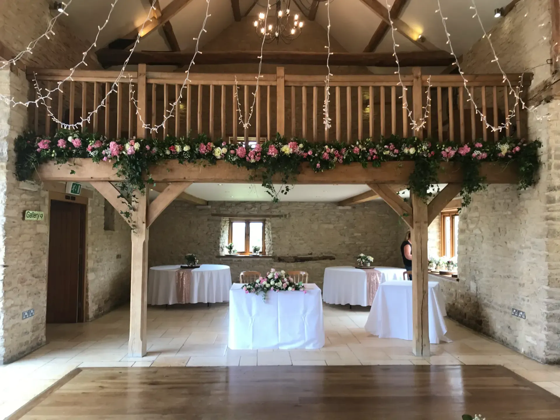 Rustic barn reception hall with white-draped tables, floral garland, and string lights above a wooden floor.