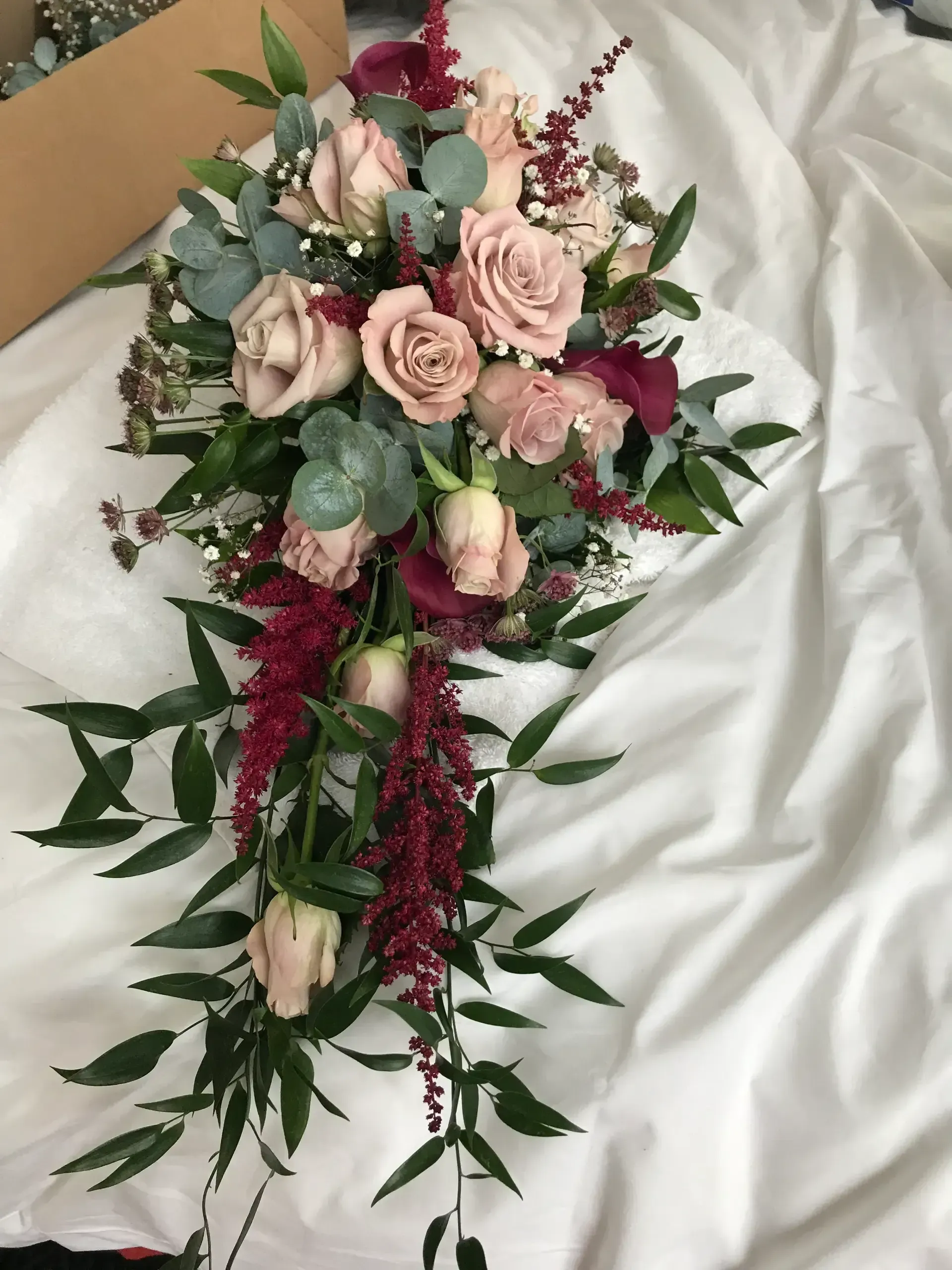 Pink and burgundy floral funeral spray with cascading greenery on white satin background
