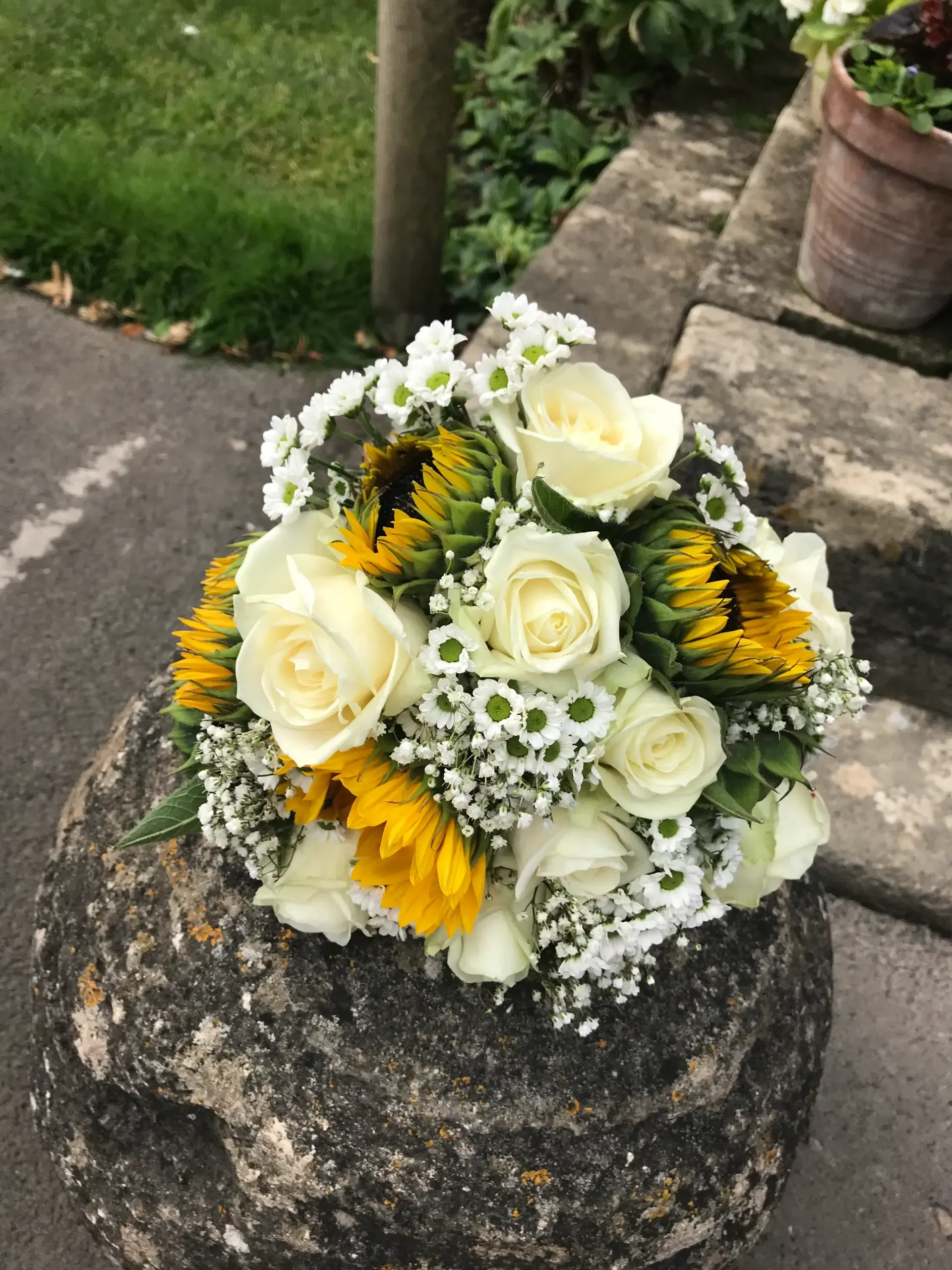 White roses and yellow sunflowers arranged in a bouquet on a stone post outdoors