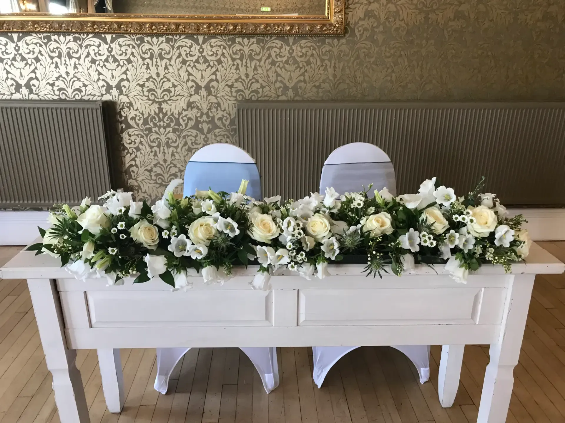 White floral arrangement on a table with two white chairs and blue and white decor behind it