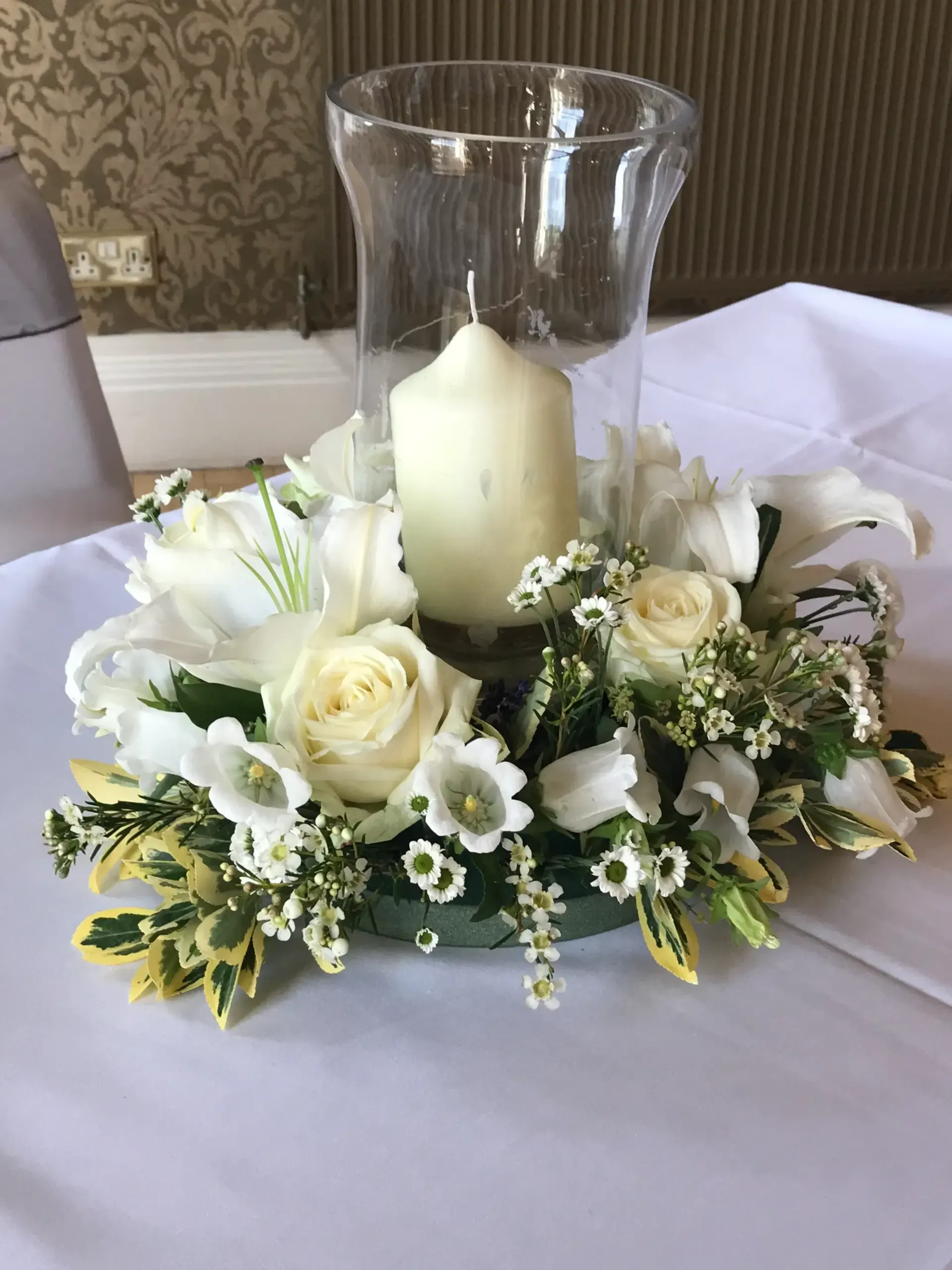 White floral centerpiece with candle in a glass vase on a table