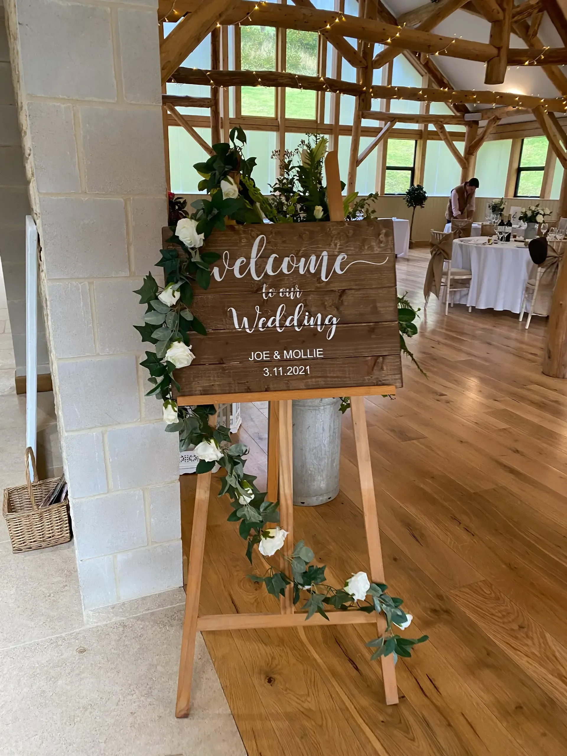 Wedding welcome sign on easel with greenery in a rustic indoor venue