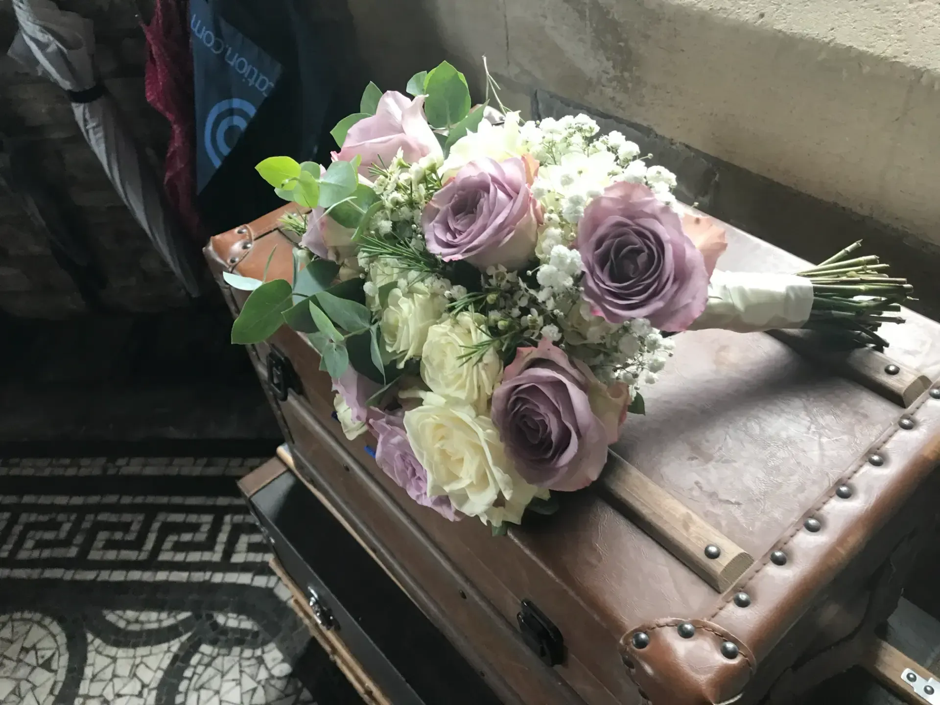 Lavender and white bouquet resting on a brown tufted chest by a window