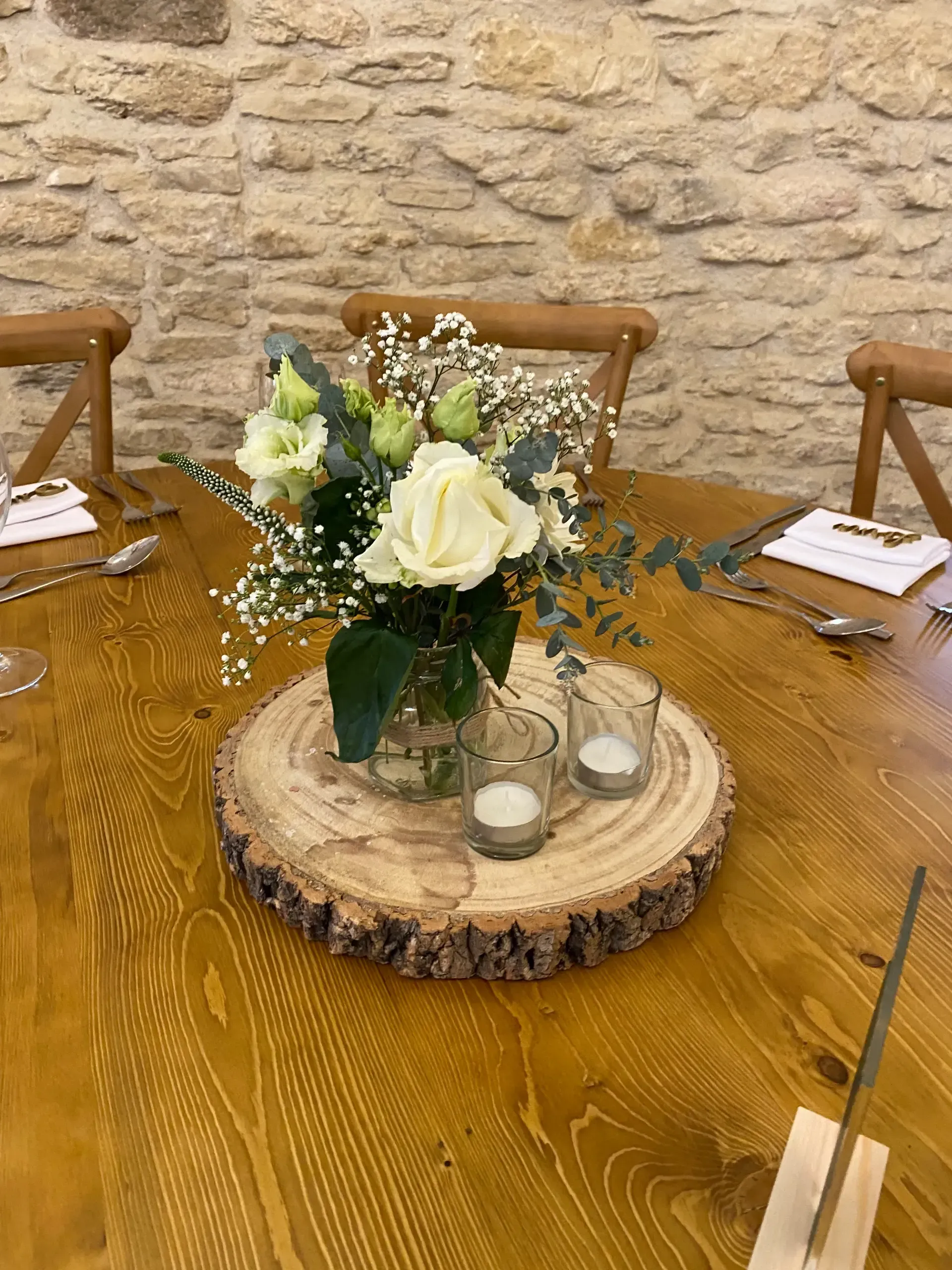 Flower centerpiece on a wooden table with stone wall backdrop and place settings
