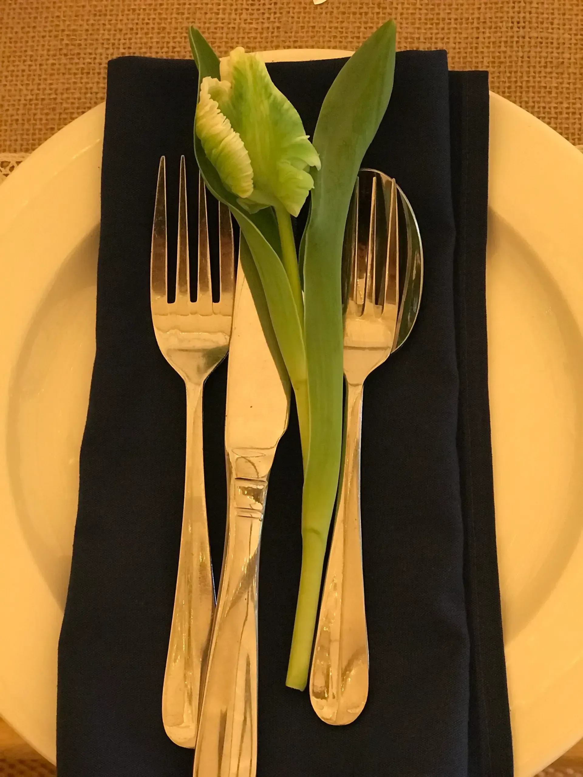 Fork and knife on a black napkin with a green leaf garnish on a beige table.