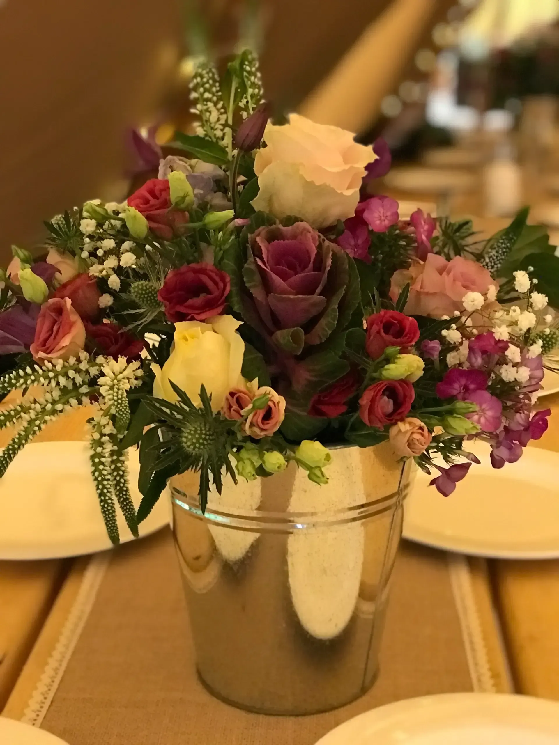 Floral centerpiece in a metal bucket with purple, red, white, and pink flowers on a banquet table