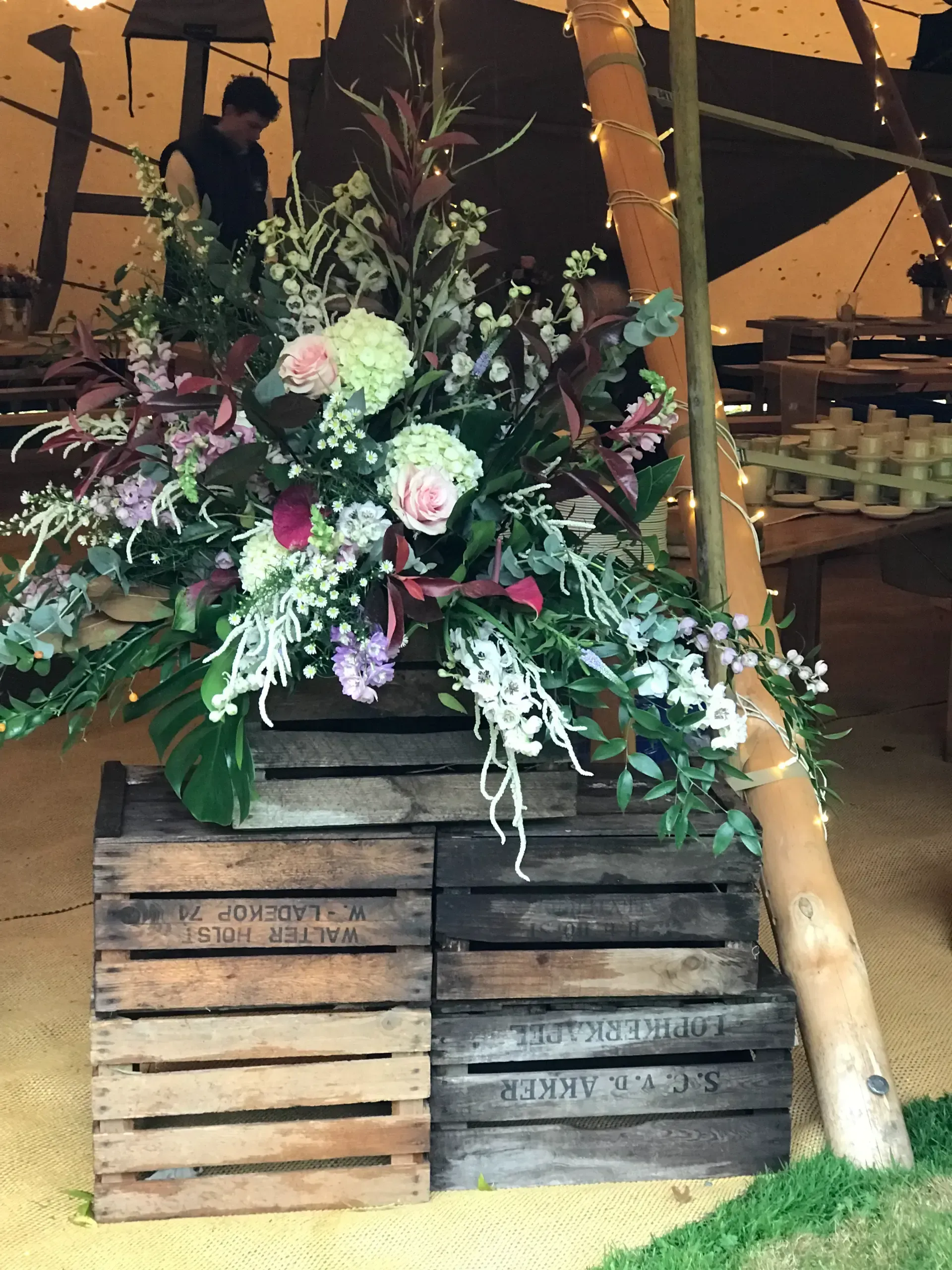 Floral arrangement with pink and white flowers on stacked wooden crates in a tented event space