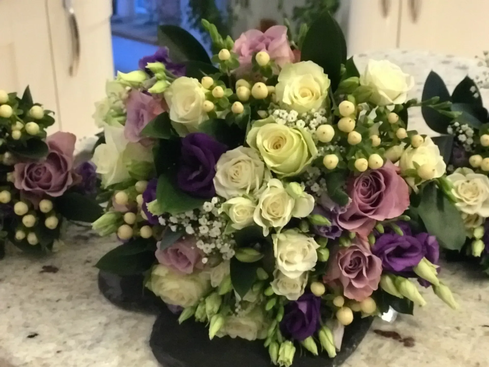 Bouquet of white, lavender, and purple roses with greenery on a table