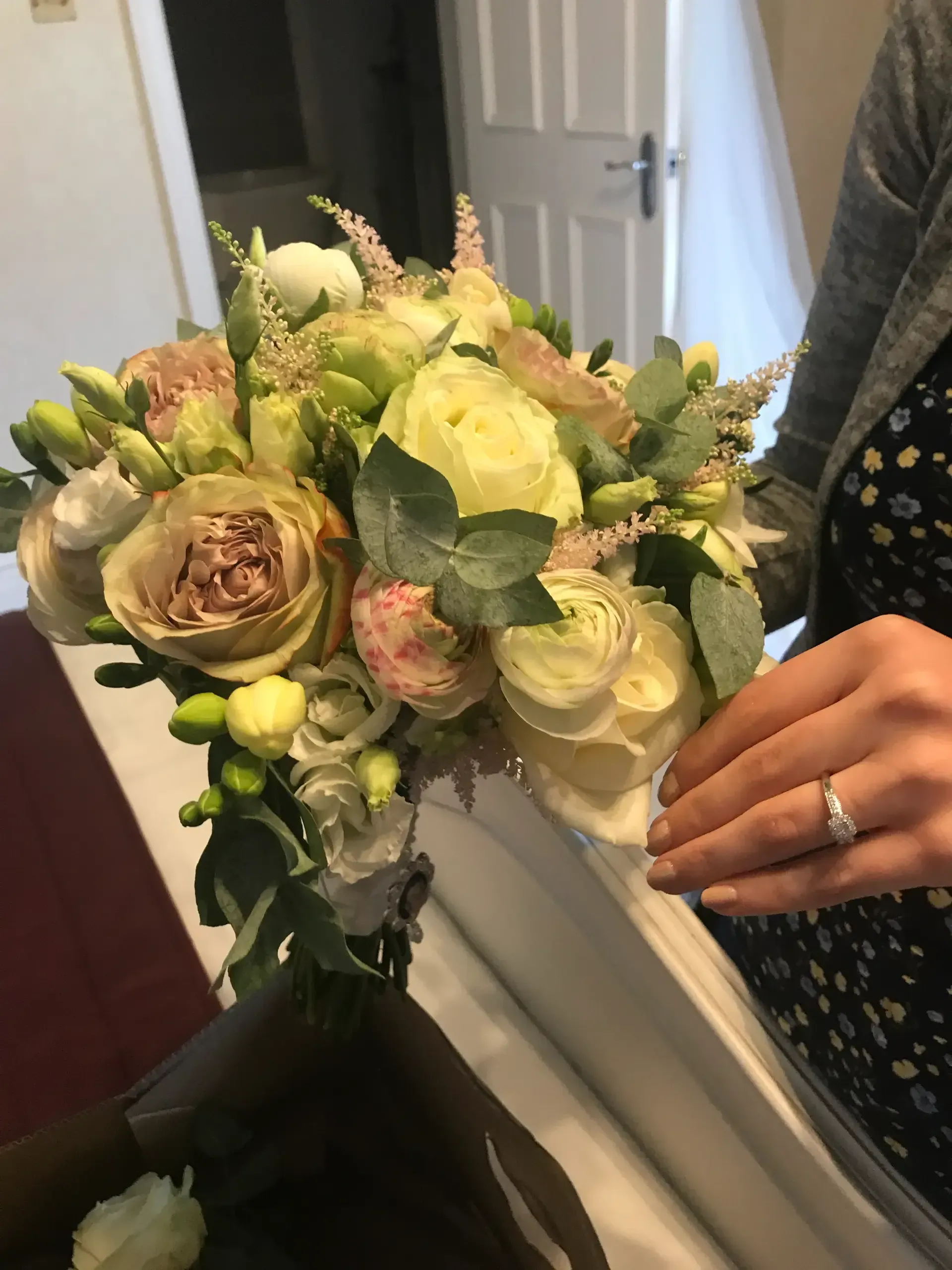 Hand holding a pale green and cream rose bouquet in a doorway