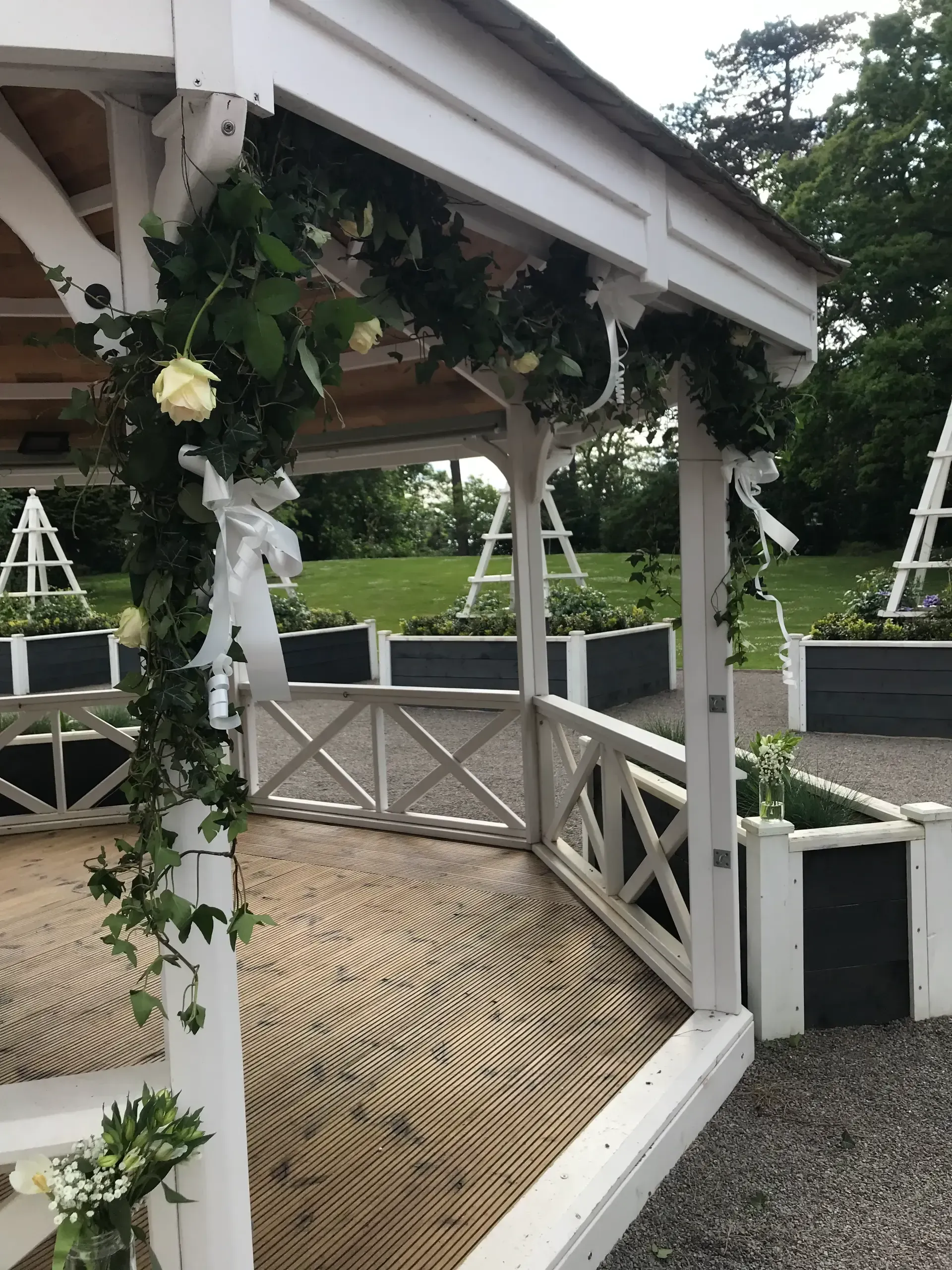 Decorated white gazebo with floral garlands and woven floor in a grassy outdoor venue