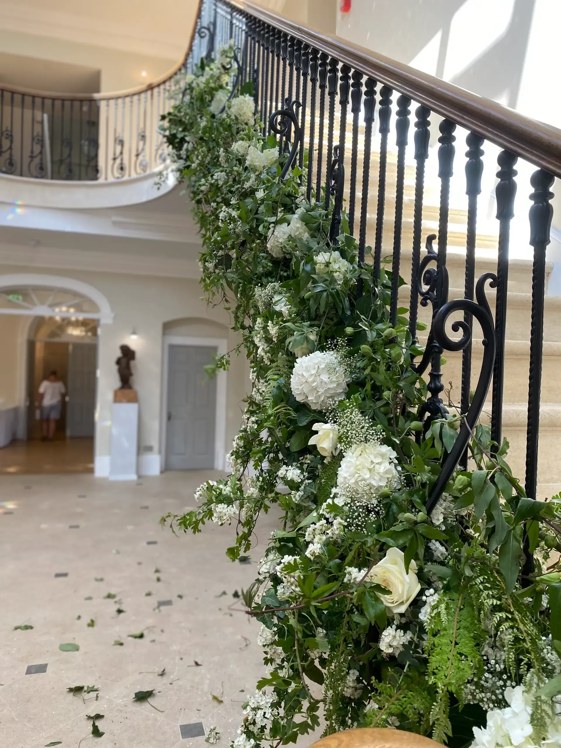 Flower garland draped along a black staircase railing in a bright, elegant foyer