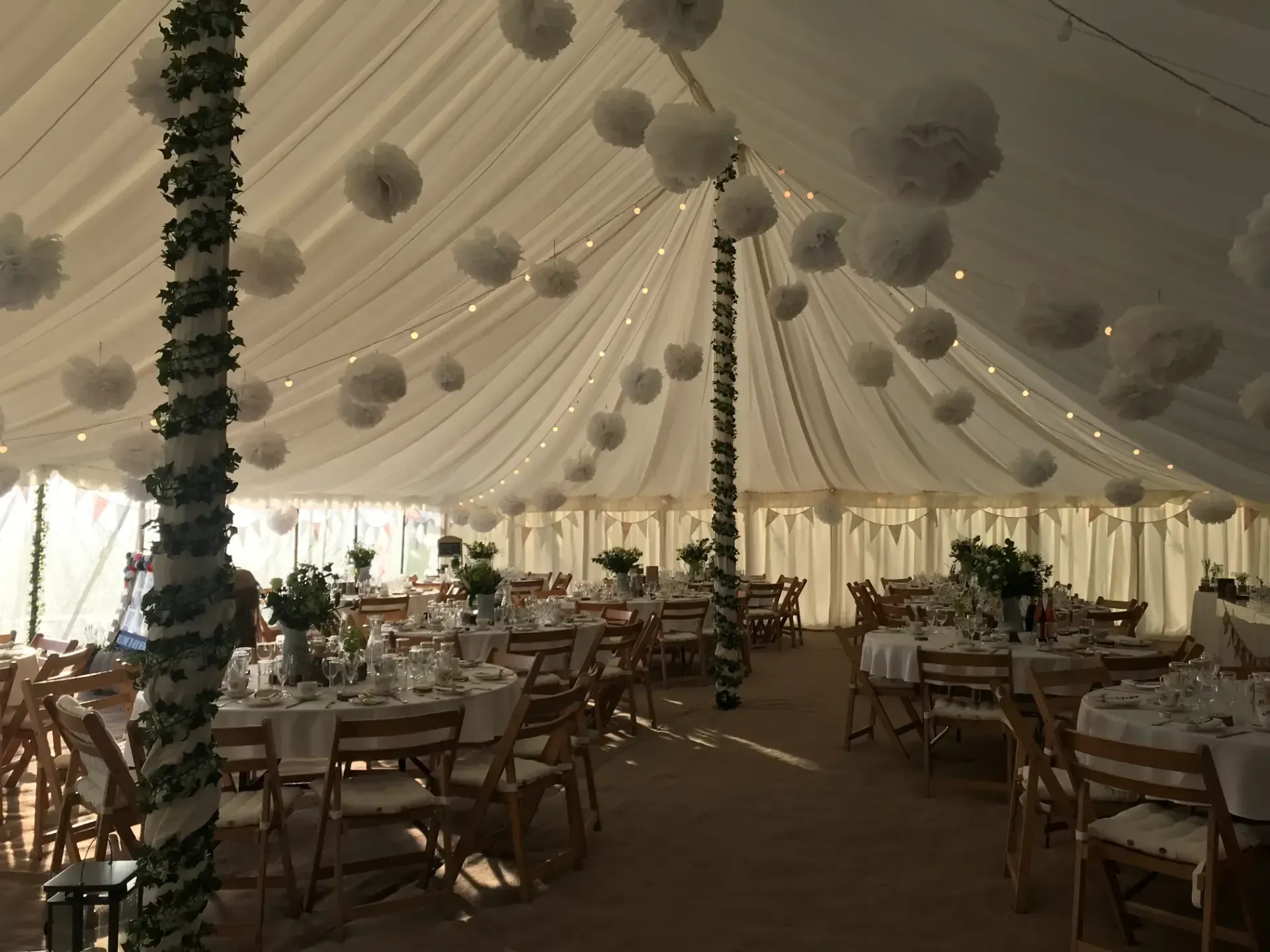 Decorated event tent with banquet tables, white drapes, and hanging floral pom-poms