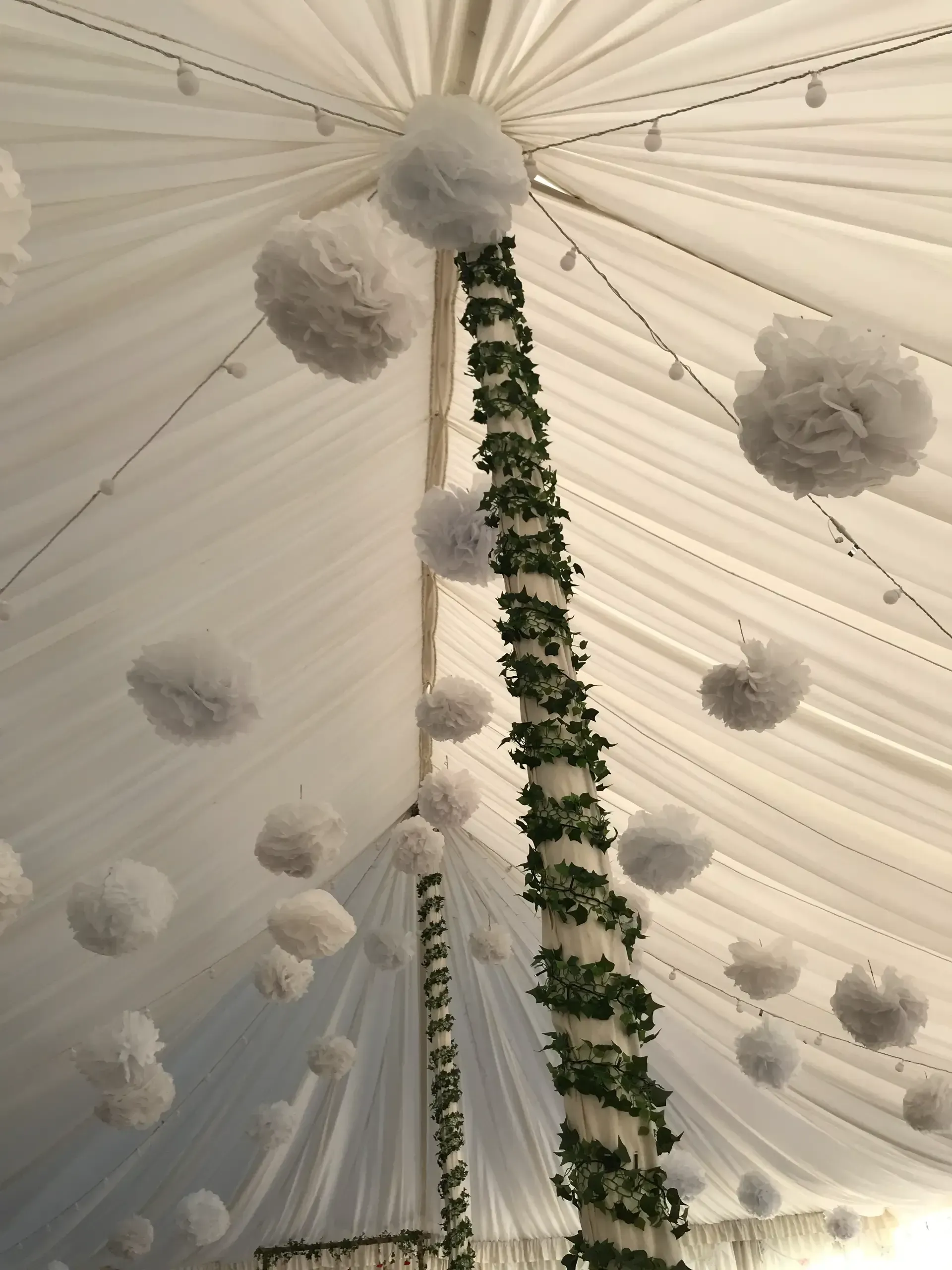 White draped tent ceiling with hanging floral garlands and fluffy pom-pom decorations