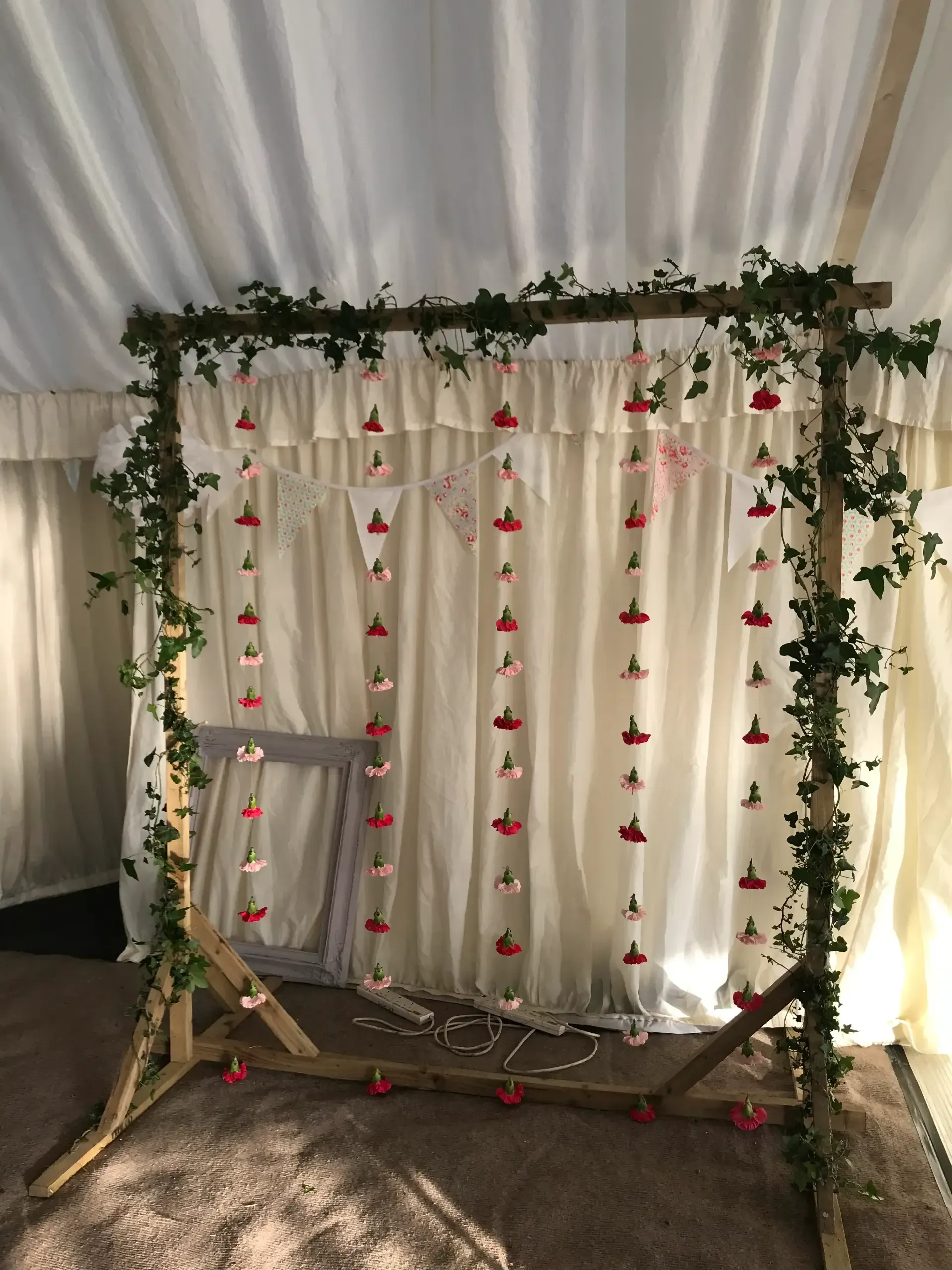 Decorated white wedding arch with greenery and hanging red ornaments in a tented event space