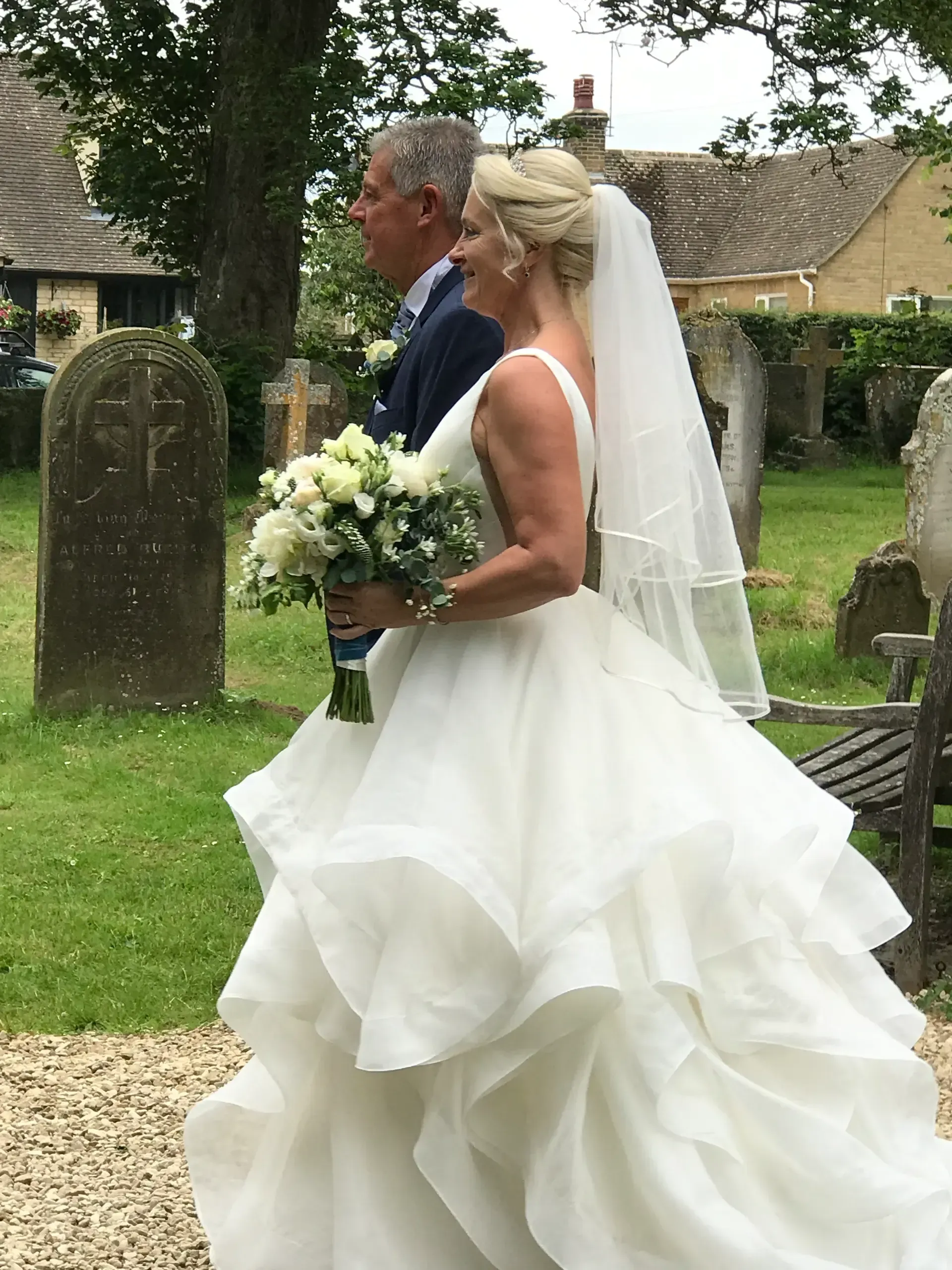 Bride and groom walking outdoors in a garden, bride in a white gown holding a bouquet.
